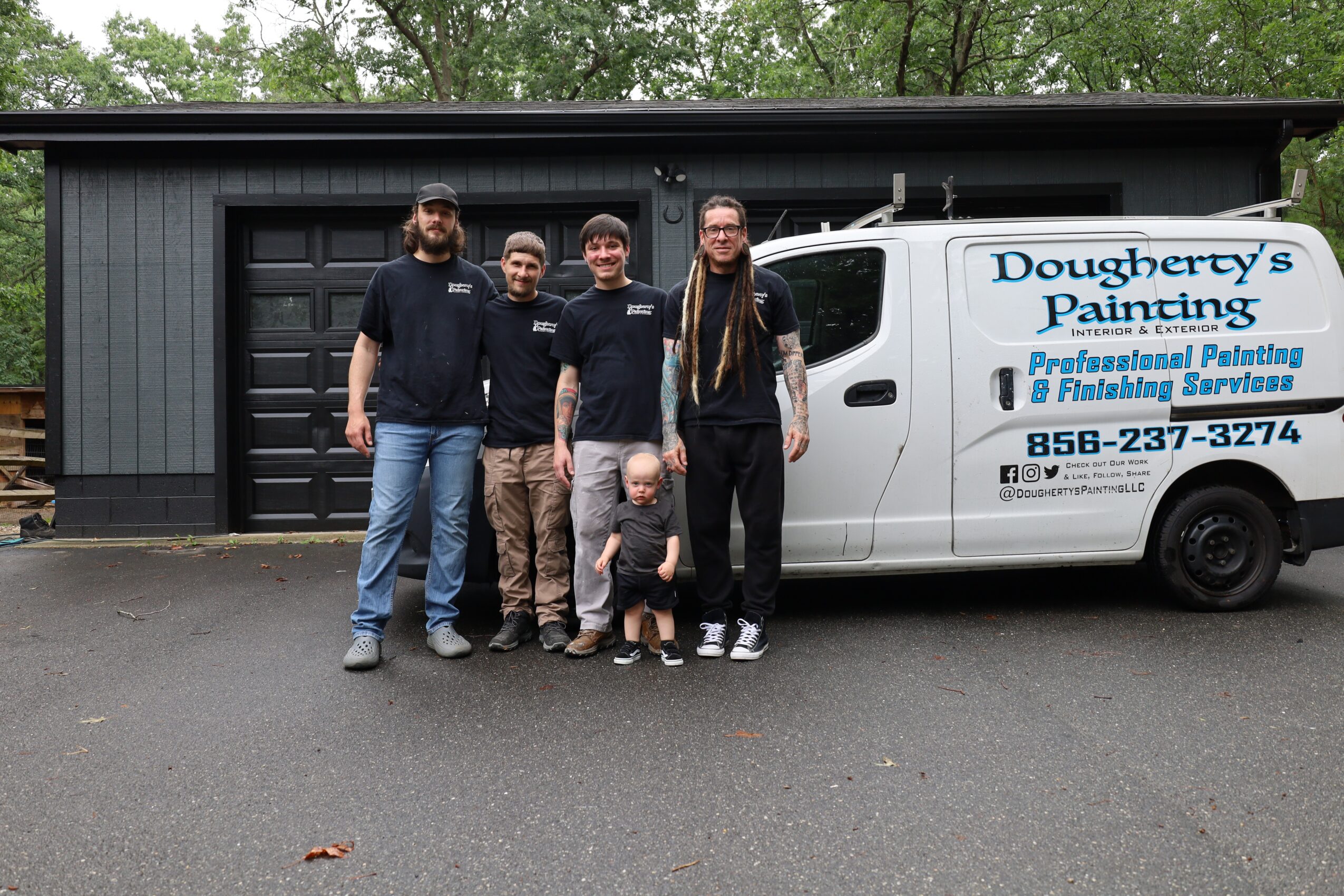 Group of five people standing in front of a building and a white van with business signage, on a paved surface.