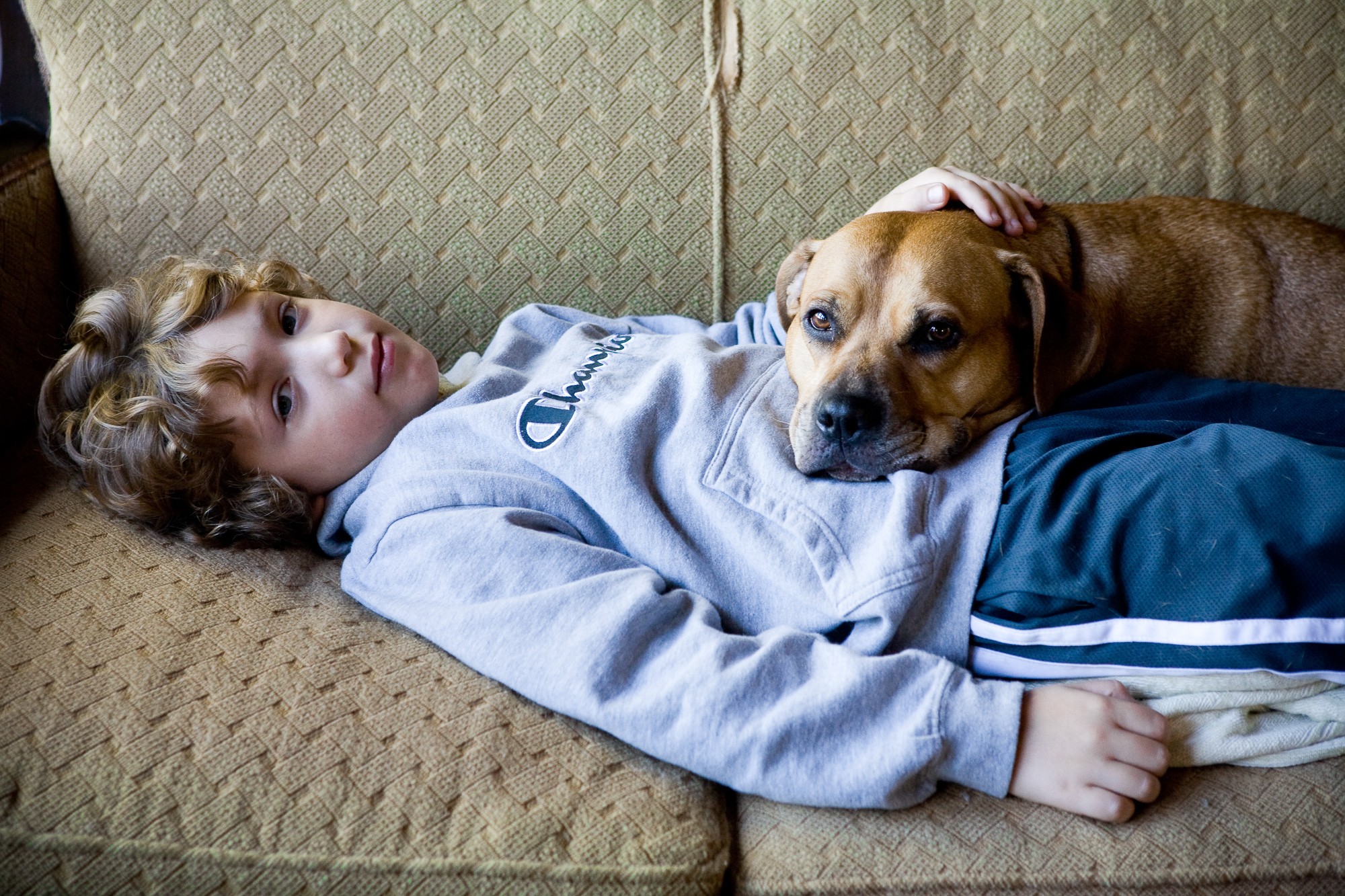 Child lying on a couch with a dog resting its head on the child's stomach, both looking at the camera.