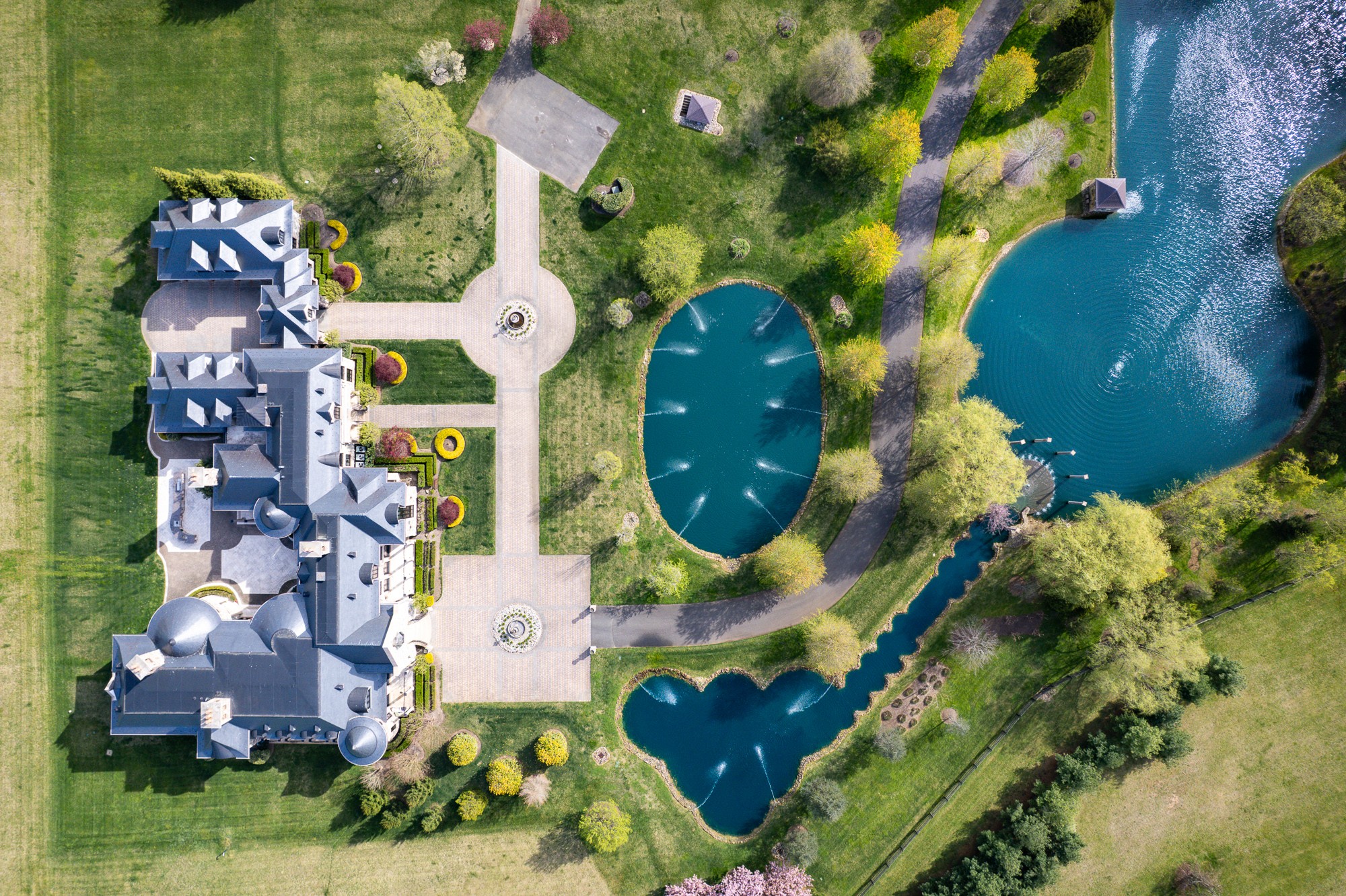 Aerial view of a large house with a garden, two ponds, and surrounding trees and lawn.