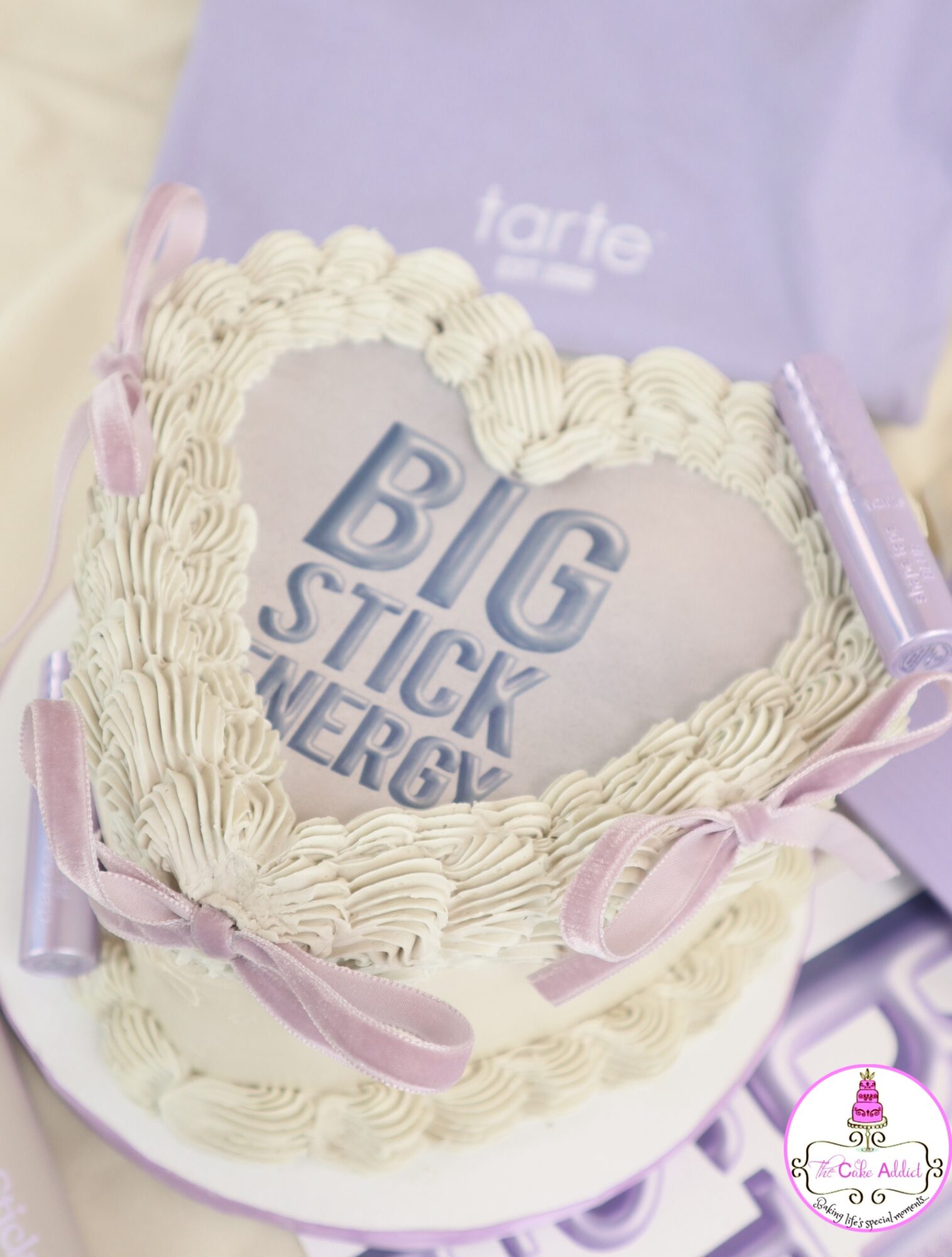 Heart-shaped cake with cream frosting and pink ribbons, with a message inside reading 'BIG STICK ENERGY'.