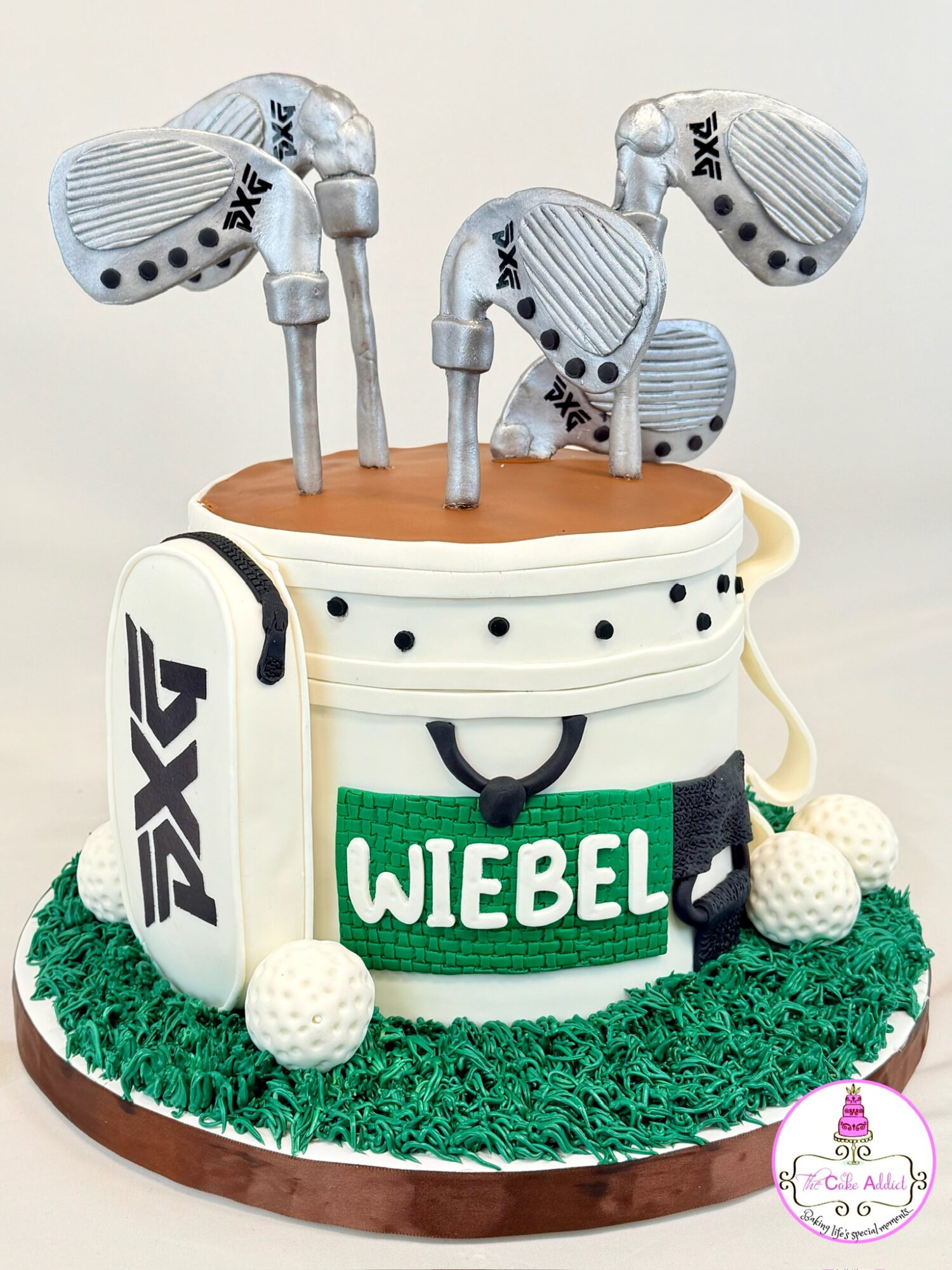 Golf-themed cake with golf clubs, a bag labeled 'WIEBEL,' and green grass decoration, on a round base.