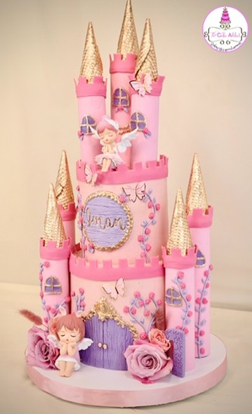 Pink castle cake with golden towers, fairy figurines, and decorative roses, celebrating a special occasion, with a unicorn and castle theme.