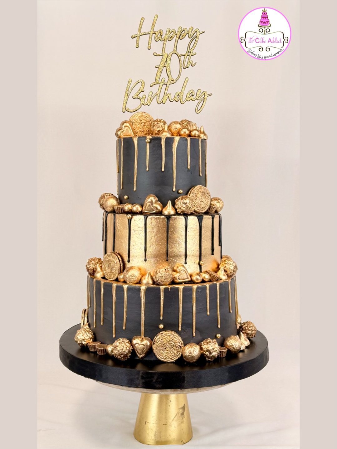 Three-tiered birthday cake with black and gold decorations, gold drips, and a topper reading 'Happy 70th Birthday'.