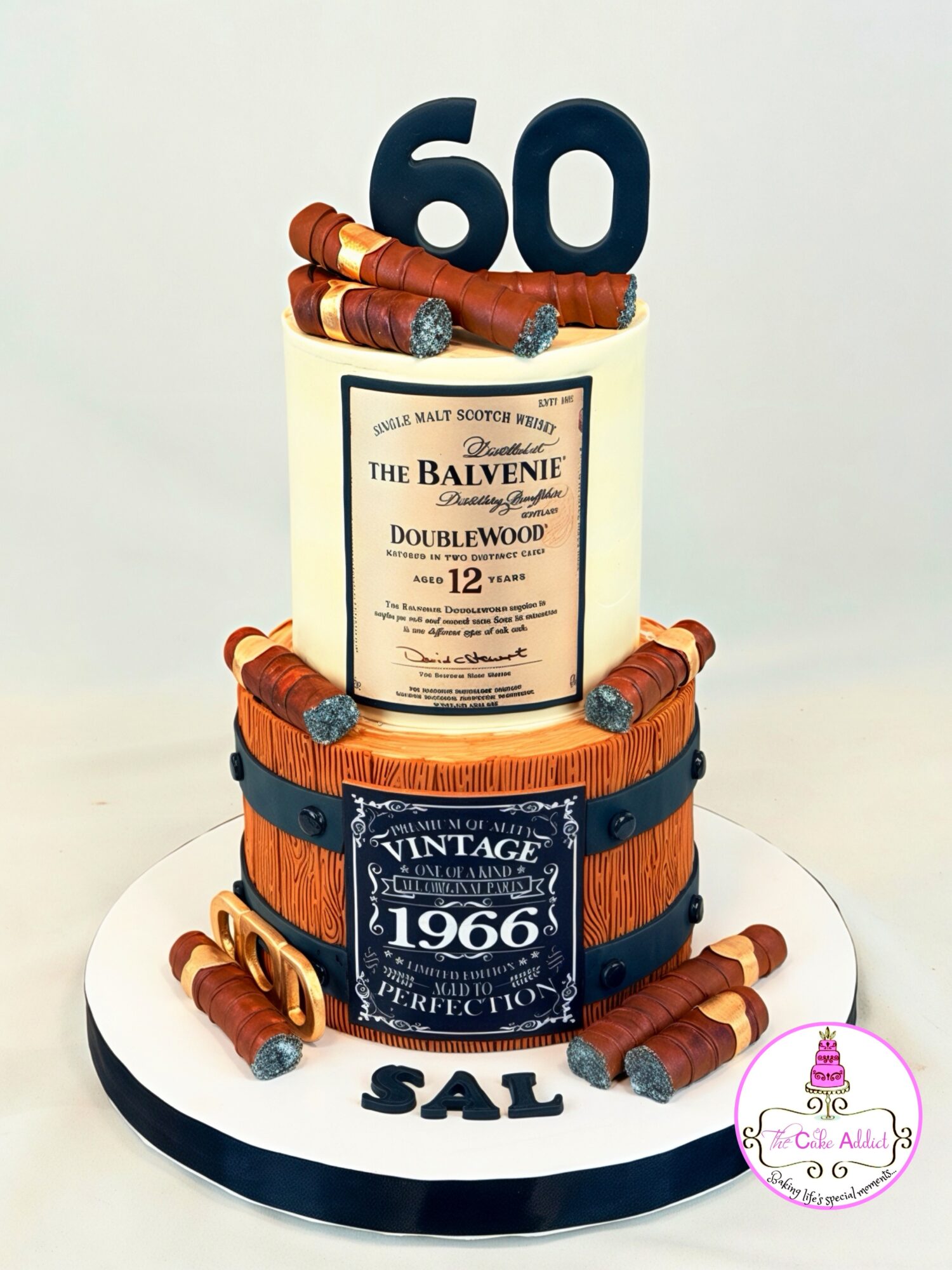 Two-tiered cake with a whiskey bottle topper, large number 60, and cigars, on a white base with 'SAL' written.