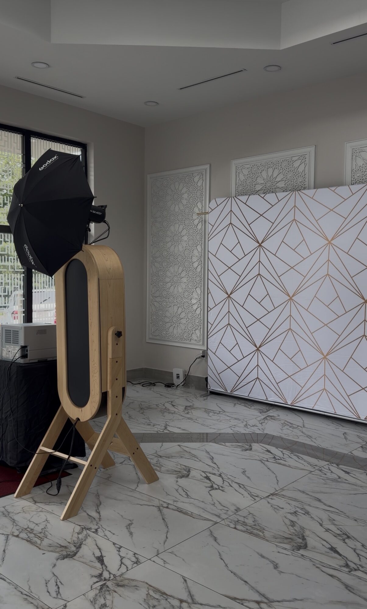 Photograph of an indoor space with a large patterned screen, a window, and a wooden object with a black attachment, marble floor.
