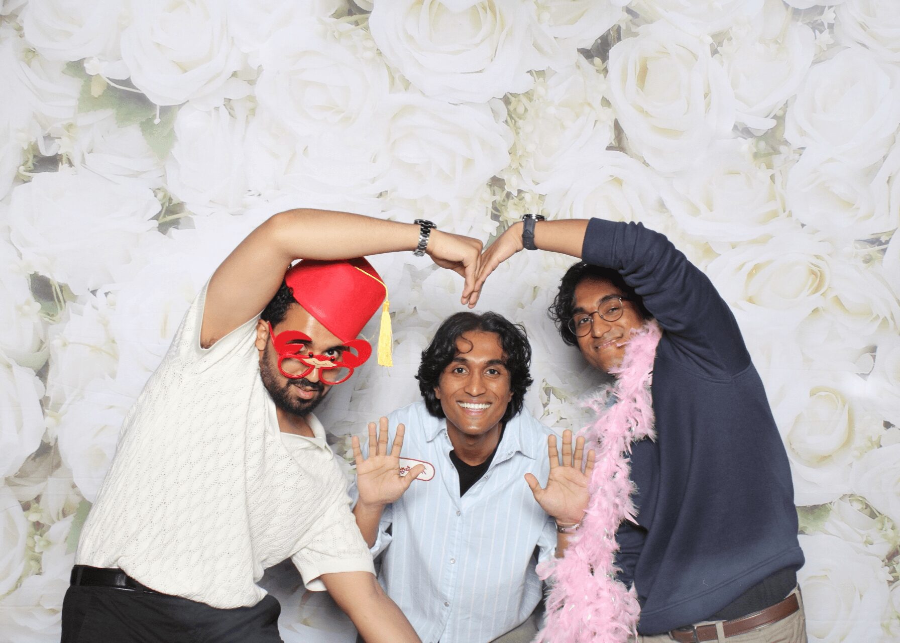 Three people smiling and posing with arms raised, standing in front of a white floral backdrop.