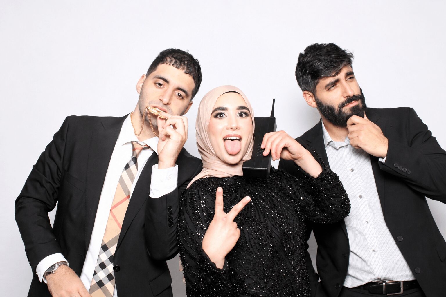Three people posing together, one woman in the middle making a peace sign and sticking out her tongue, two men on either side, all in formal attire.