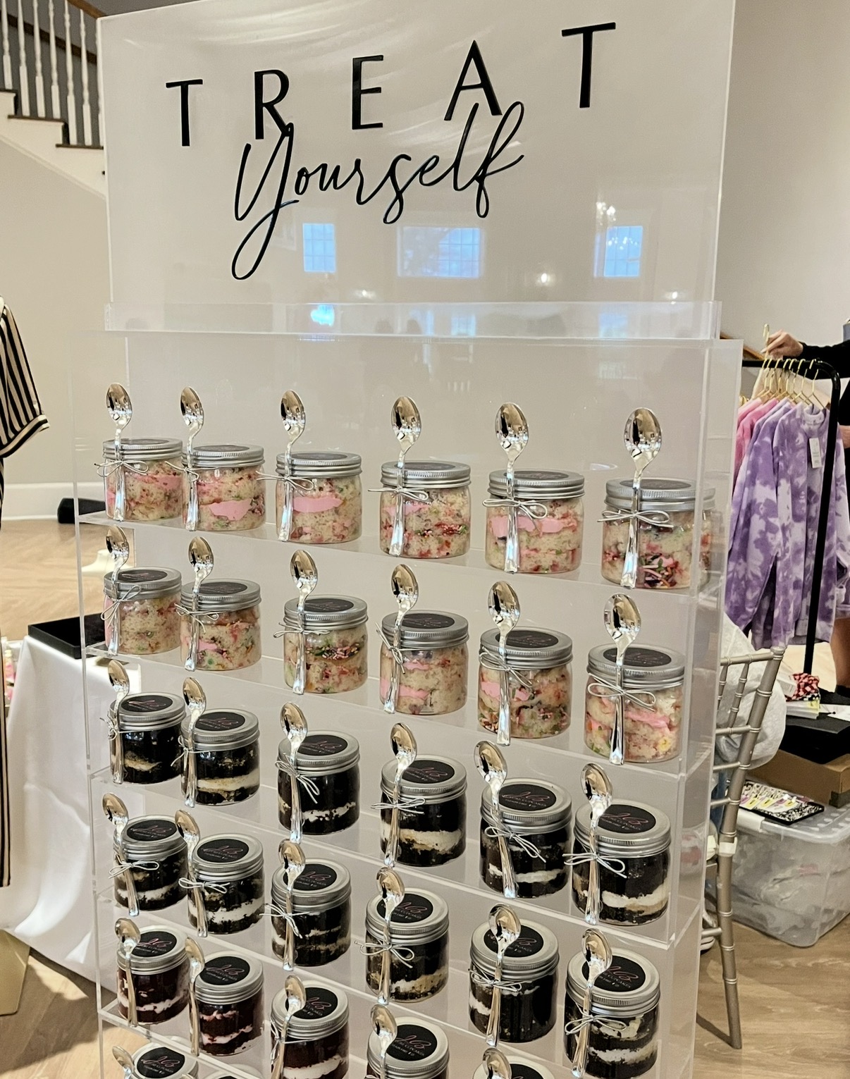 Display of small jars with spoons, arranged in rows, with a sign reading 'TREAT Yourself' above. The jars contain various desserts.