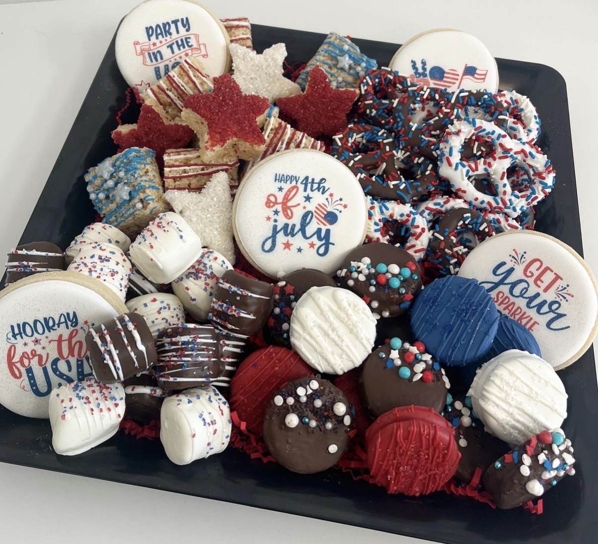 Tray of decorated cookies and cupcakes with July 4th themes and patriotic colors, including red, white, and blue, with sprinkles and icing.