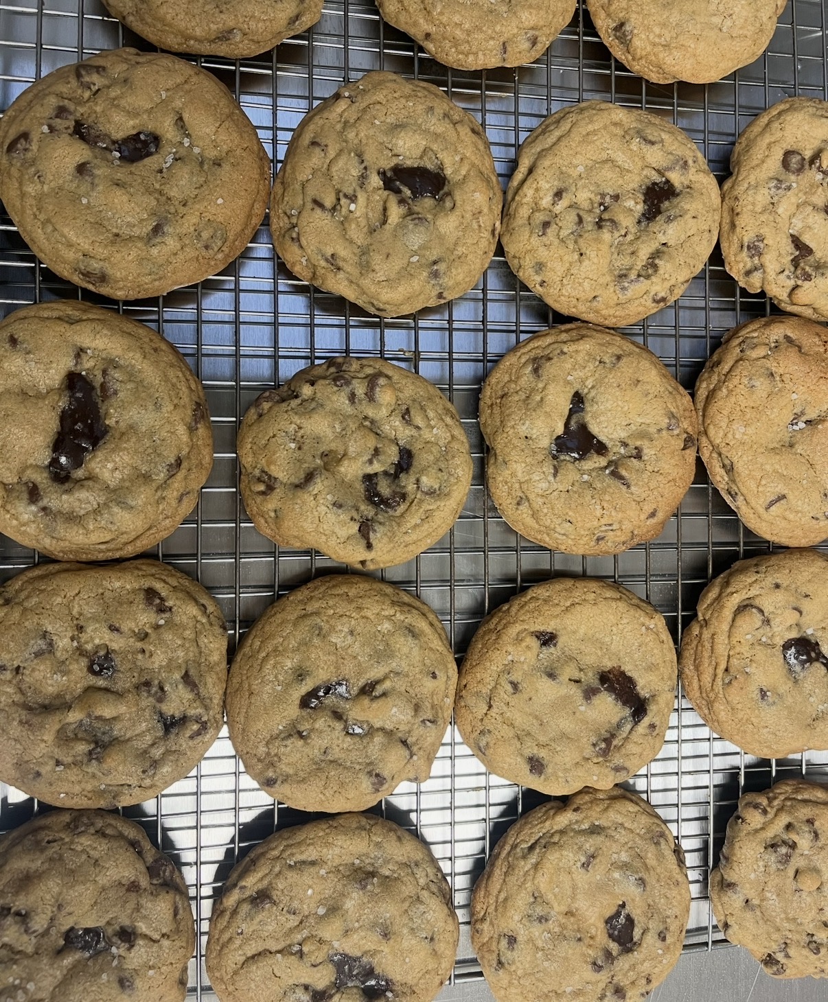Chocolate chip cookies on a cooling rack, some with visible chocolate chips, arranged in rows.