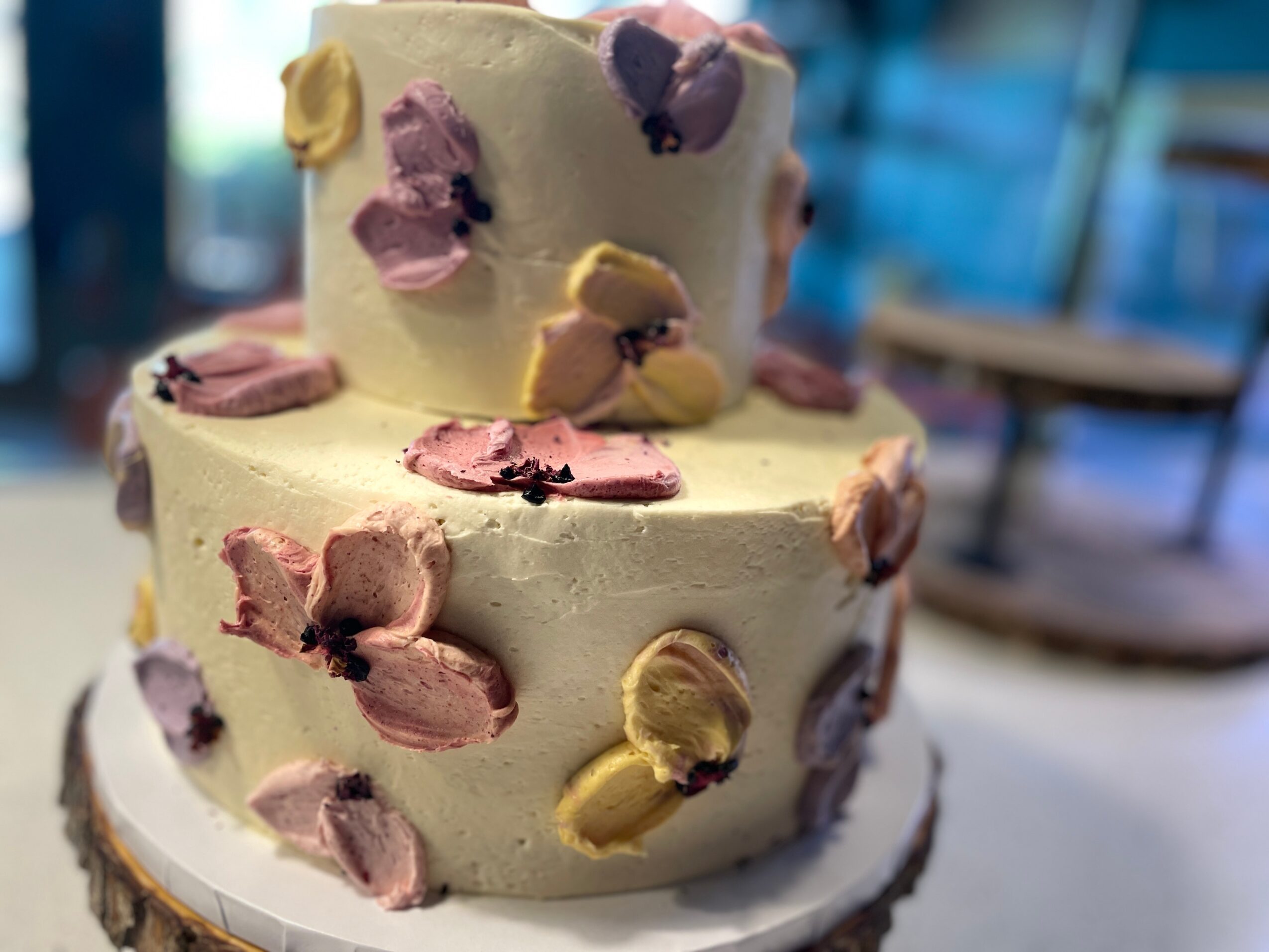 Two-tiered cake decorated with pastel-colored butterfly-shaped frosting decorations, set on a white cake board.