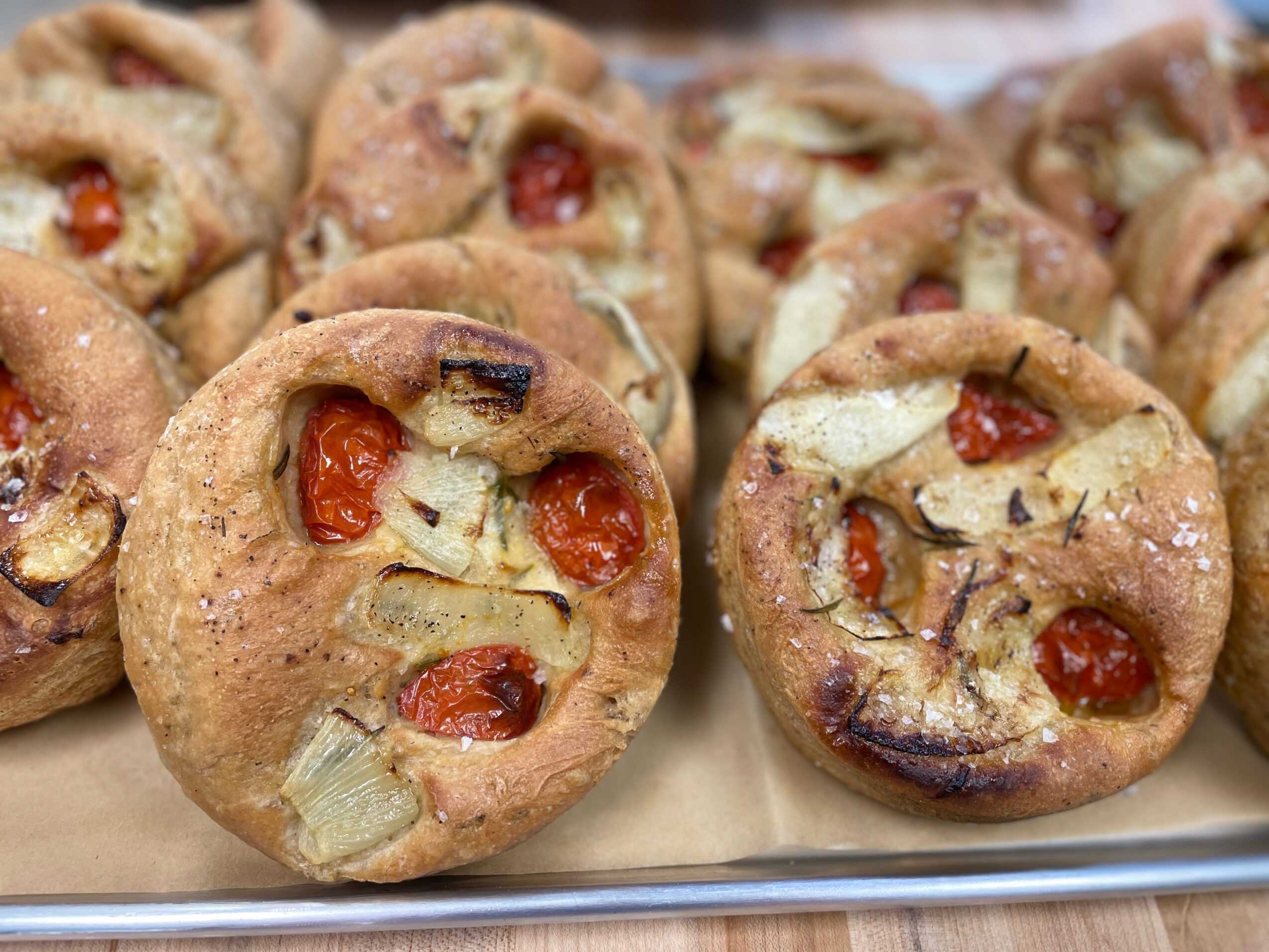 Close-up of baked savory muffins with cherry tomatoes, cheese, and herbs on a tray.
