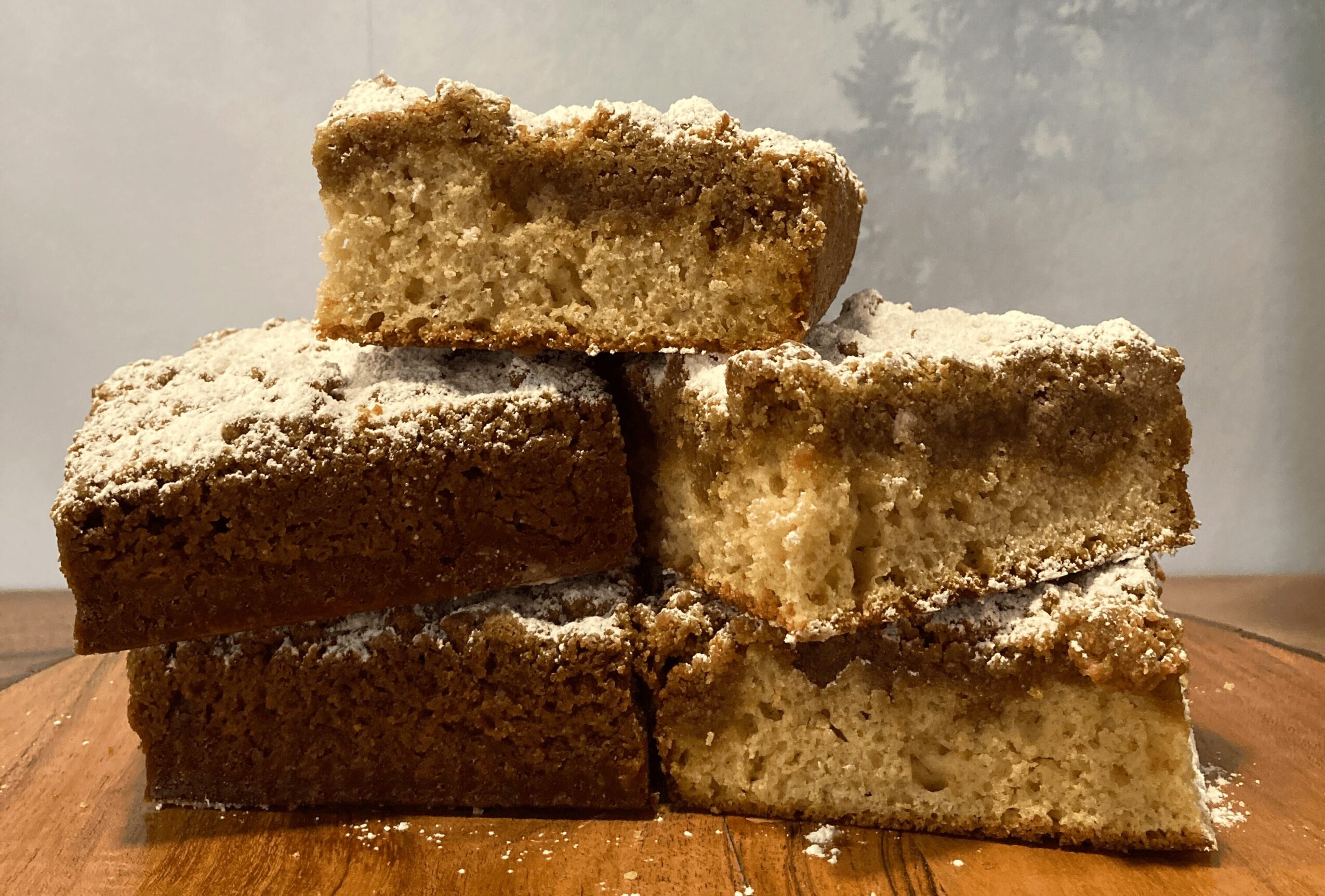 Stacked slices of cake with powdered sugar on top, placed on a wooden surface.