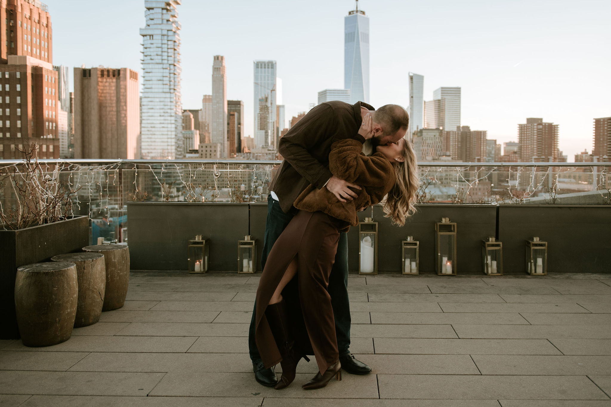 Two people embrace on a rooftop with a city skyline in the background, sunlight illuminating the scene.