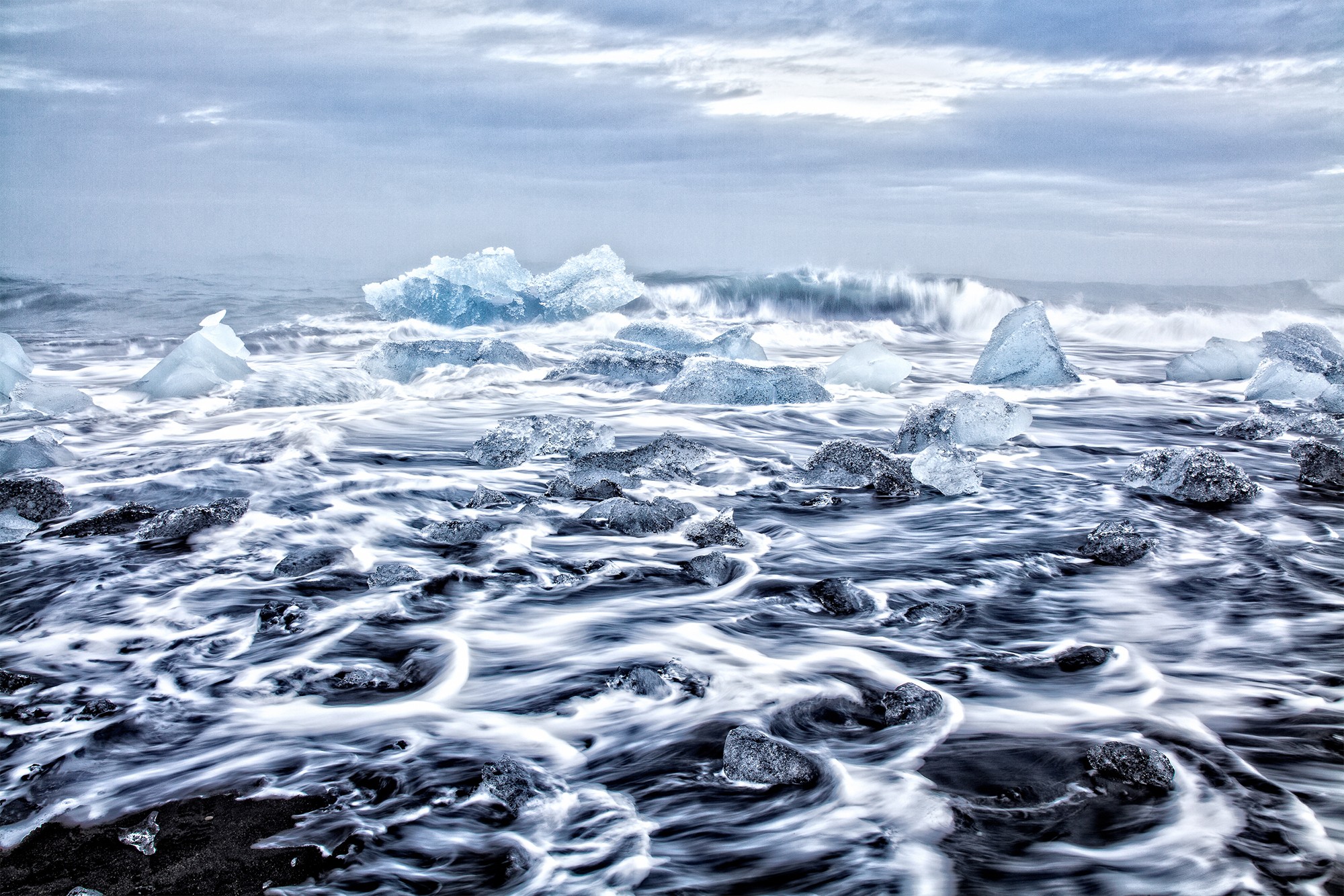 Frozen ocean with icebergs and swirling water, cloudy sky in the background.