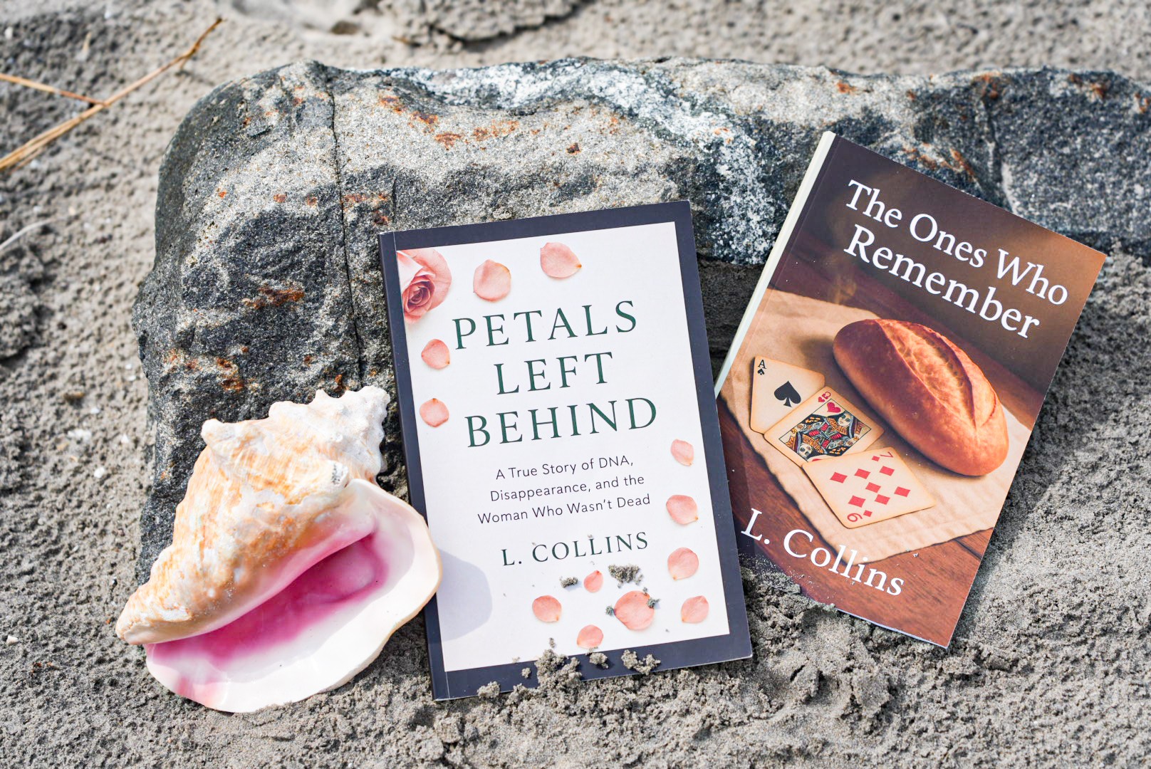 Two books and a seashell on a rock surface, with the books titled 'Petals Left Behind' and 'The Ones Who Remember'.