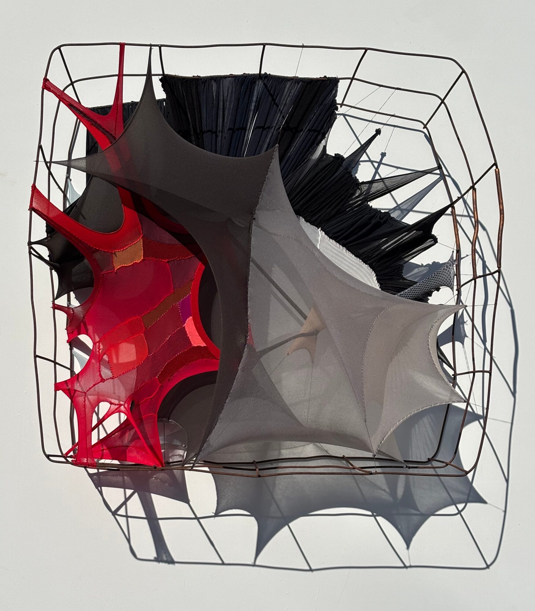 Colorful umbrellas inside a wire basket, with shadows cast on a light background.
