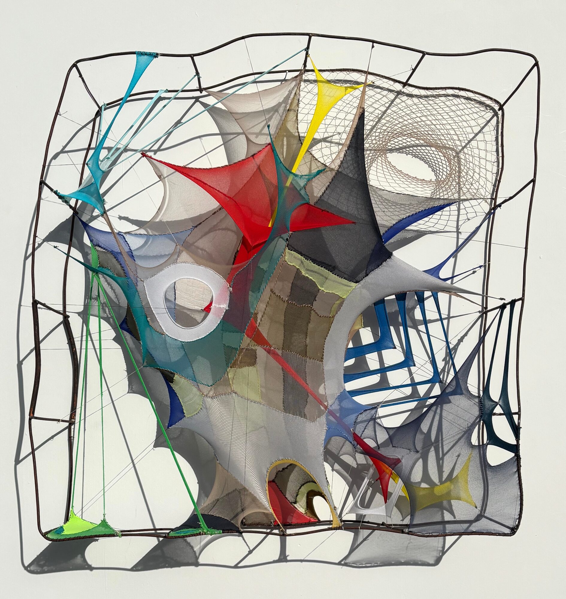 Abstract wireframe sculpture with colorful fabric shapes inside, viewed from the front, with a neutral background.