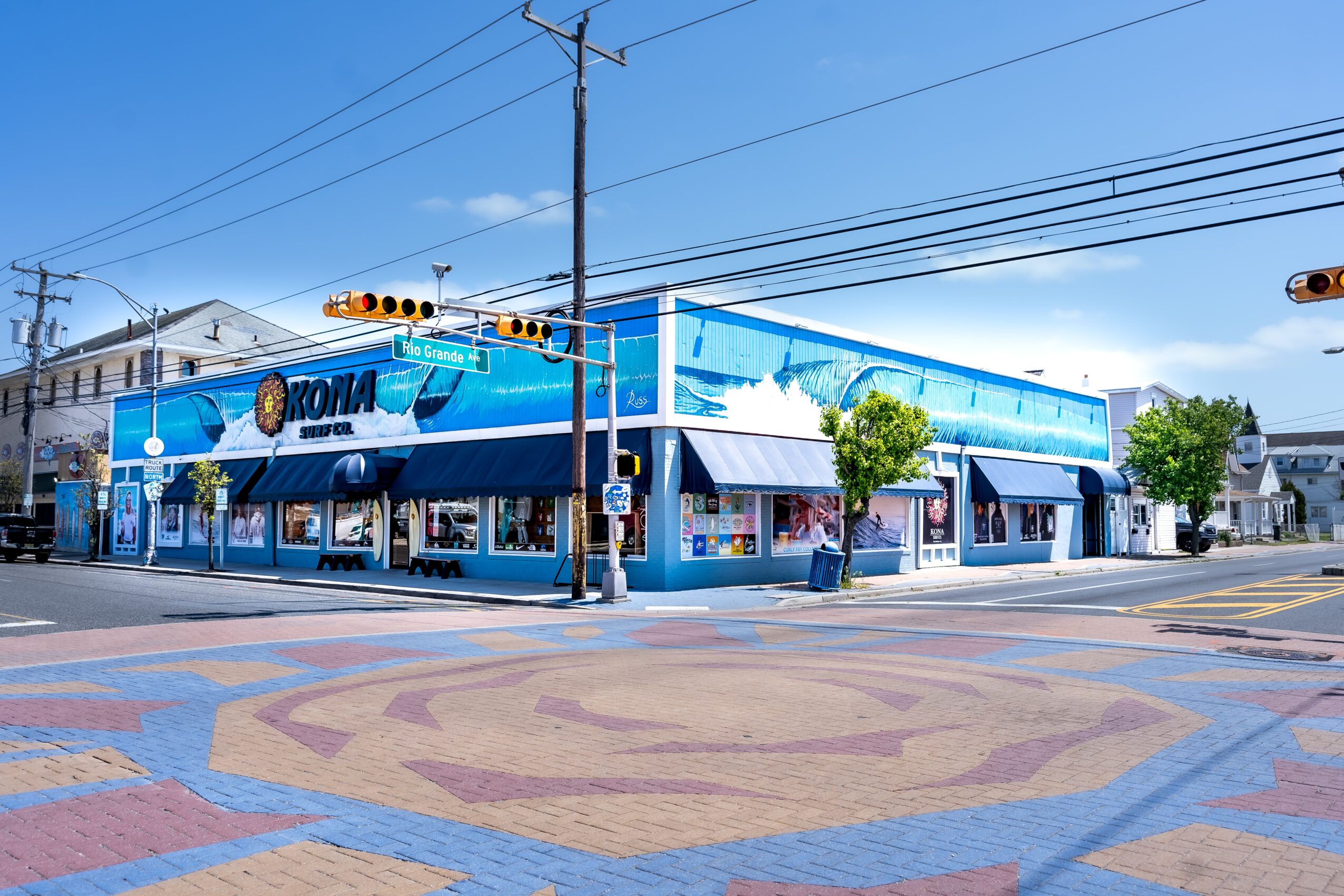 Corner building with blue exterior, street intersection, traffic lights, and power lines, under a clear blue sky.