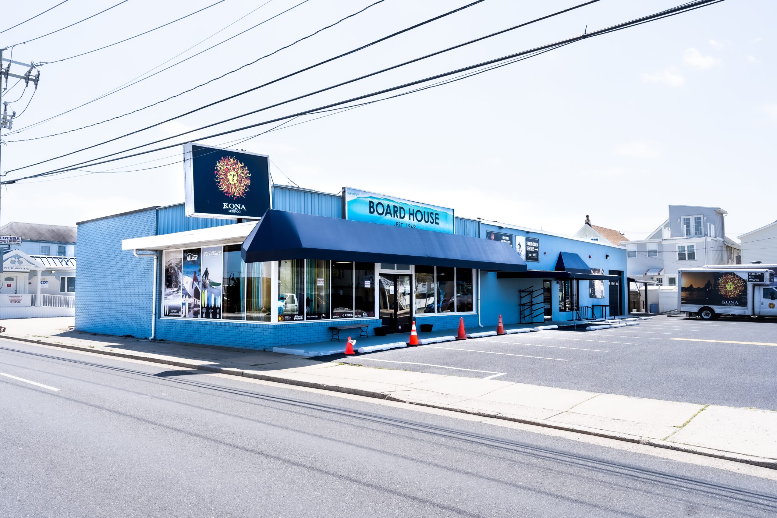 Blue building with signs reading 'BOARD HOUSE' and a logo, large windows, and a parking lot in front.