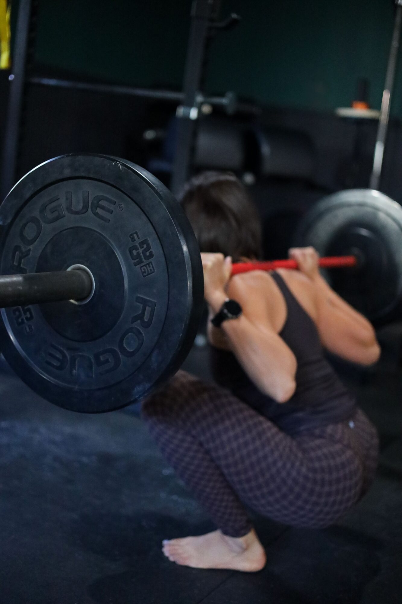 Person performing a squat with a barbell loaded with weight plates in a gym.
