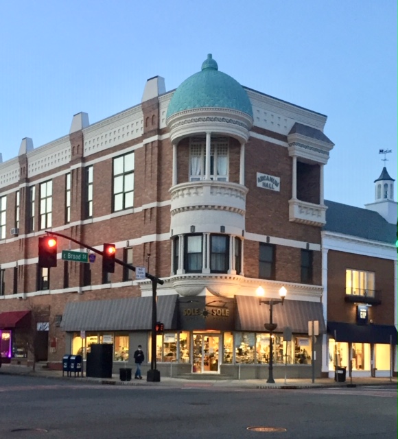Corner building with a rounded turret and green dome, storefronts at street level, streetlights, and traffic signal, daytime.