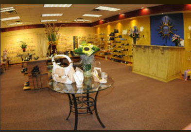Flower arrangement on a glass table in a store with yellow walls and shelves, and a blue and yellow display in the background.