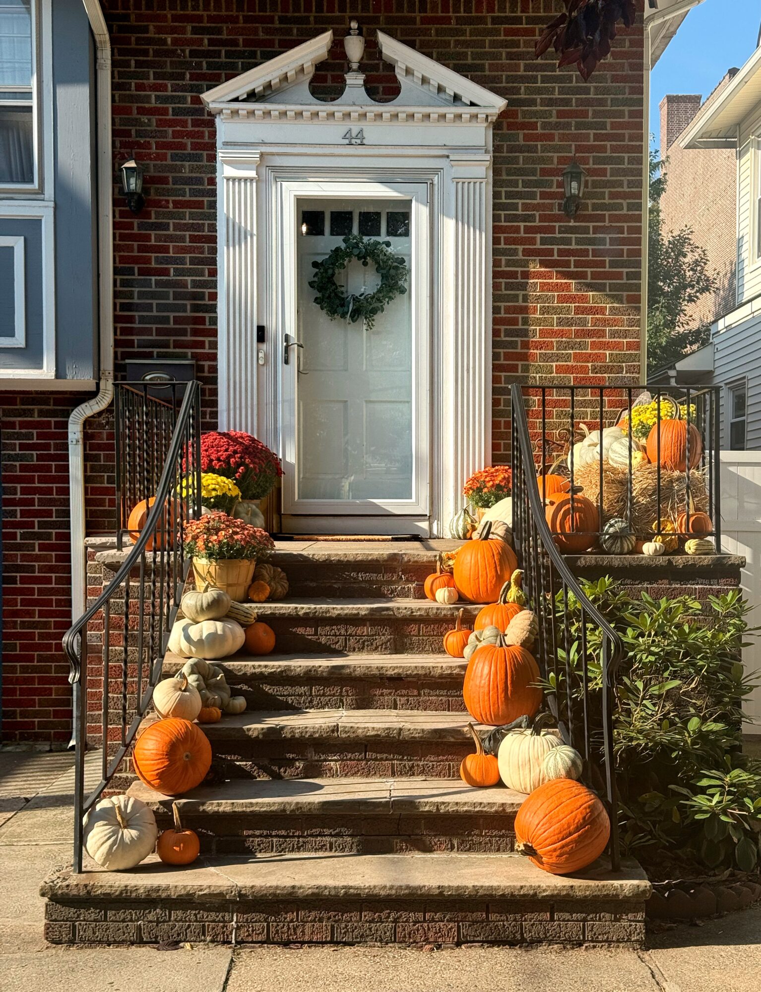 Front door decorated with pumpkins and white and orange gourds, with a wreath on the door, steps leading up to the entrance, and a brick house exterior.