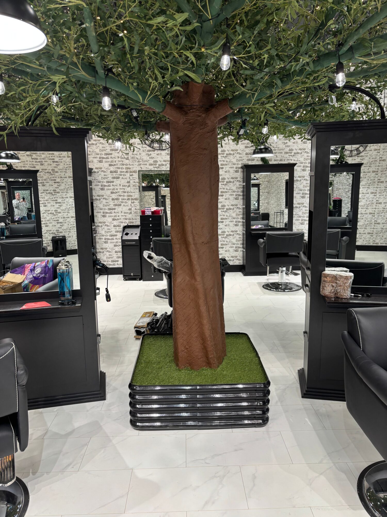 A brown artificial tree trunk with green foliage and small ornaments, placed on a green mat in a modern interior space.