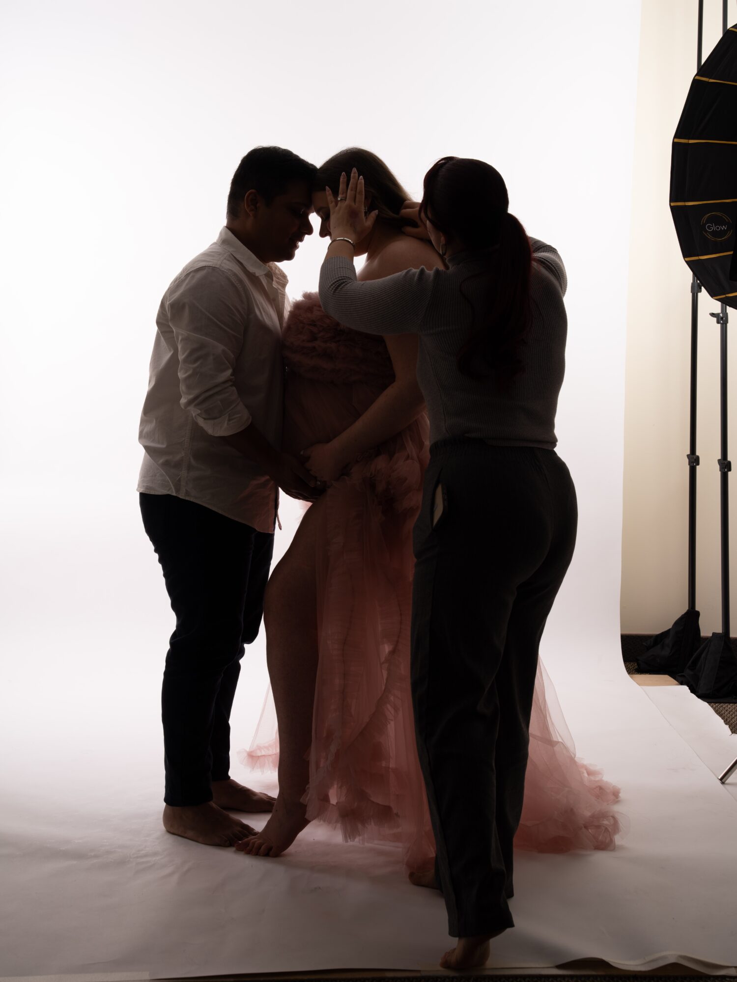 Three people, two women and one man, are in a photo shoot studio with a white background, engaged in a pose.