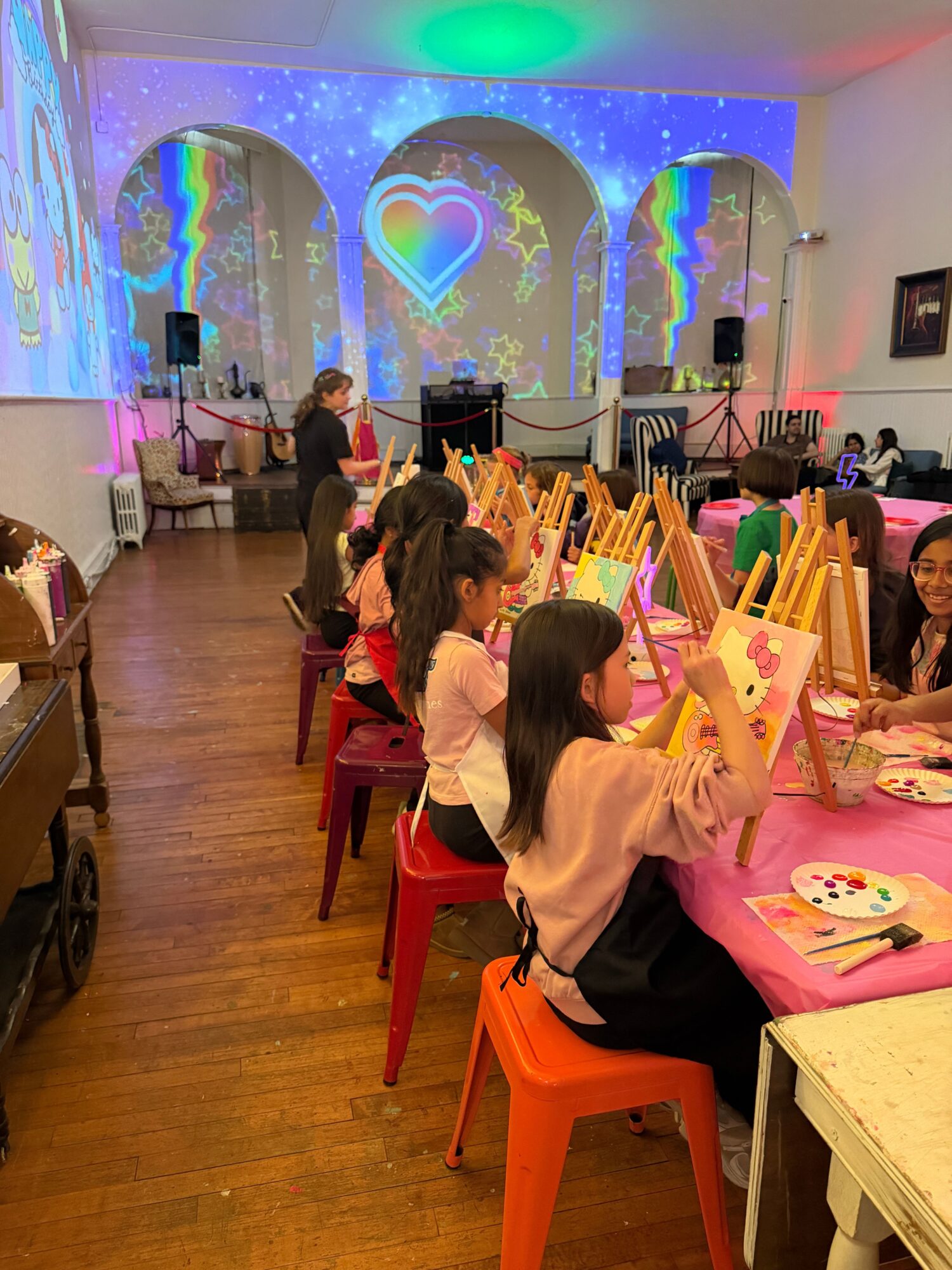 Children gather around a table with colorful decorations and gifts in a decorated room with a starry backdrop.