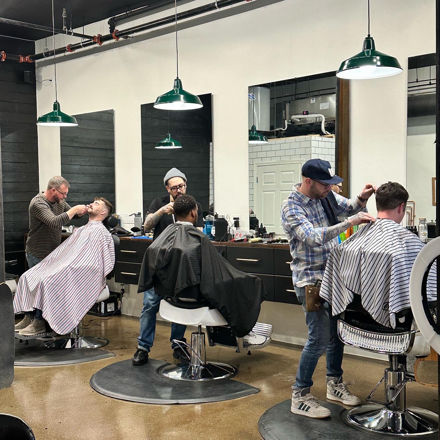 Barbershop scene with barbers cutting men's hair, mirrors, and chairs in a modern salon interior.