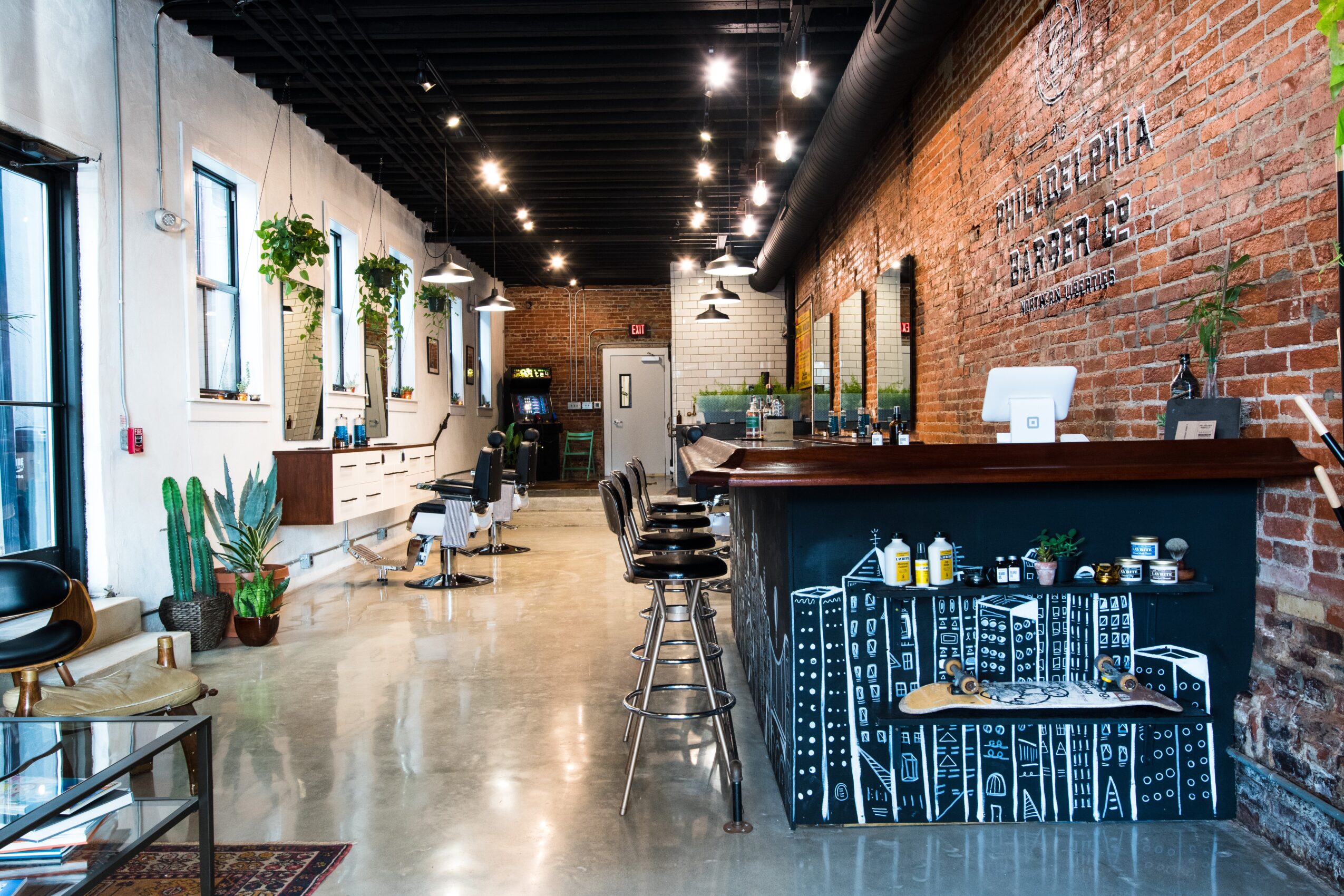 Modern cafe interior with brick and white walls, bar counter with stools, plants, and seating area, well-lit and spacious.