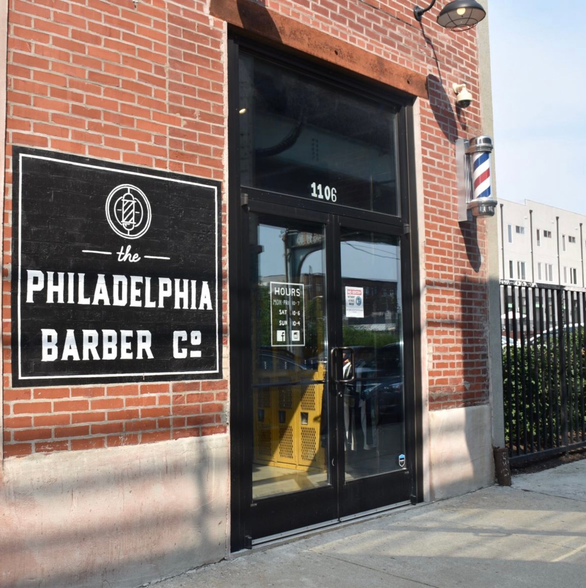 Brick building entrance with a black sign reading 'Philadelphia Barber Co.' and a glass door with the number 1106 above it.