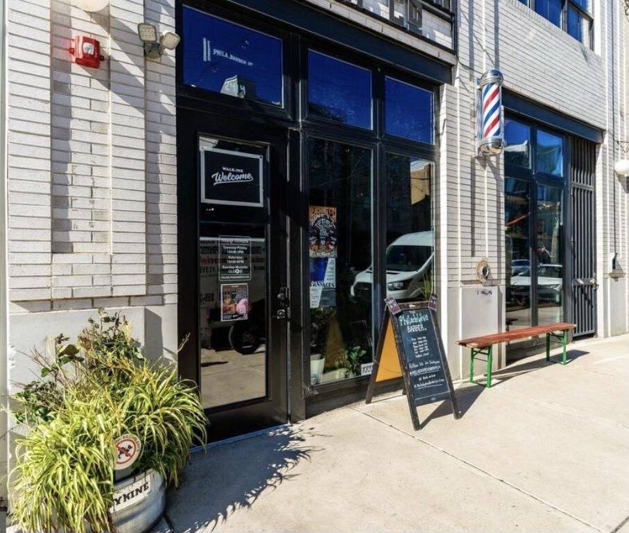 Storefront with glass door and windows, chalkboard sign outside, and a bench on the sidewalk.