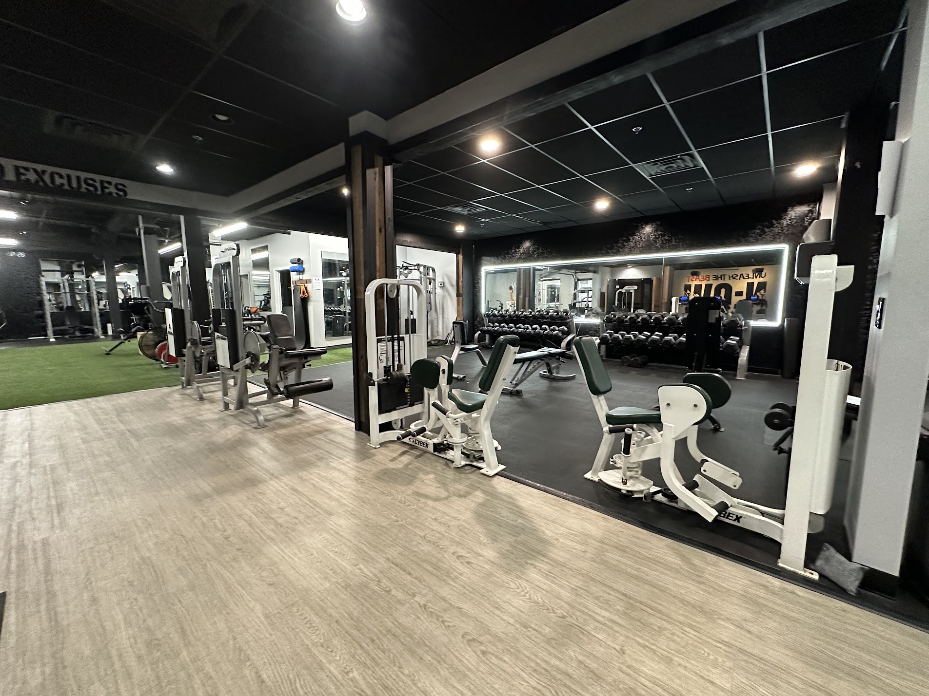 Gym with exercise machines, weights, and workout area, illuminated with ceiling lights and a black ceiling, wooden floor.