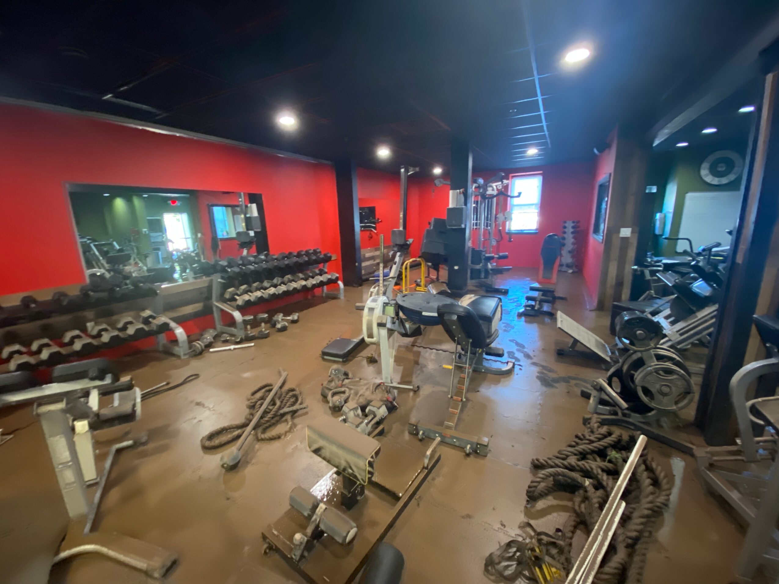 Gym with red walls, mirrors, workout equipment, and scattered ropes and weights on the floor.