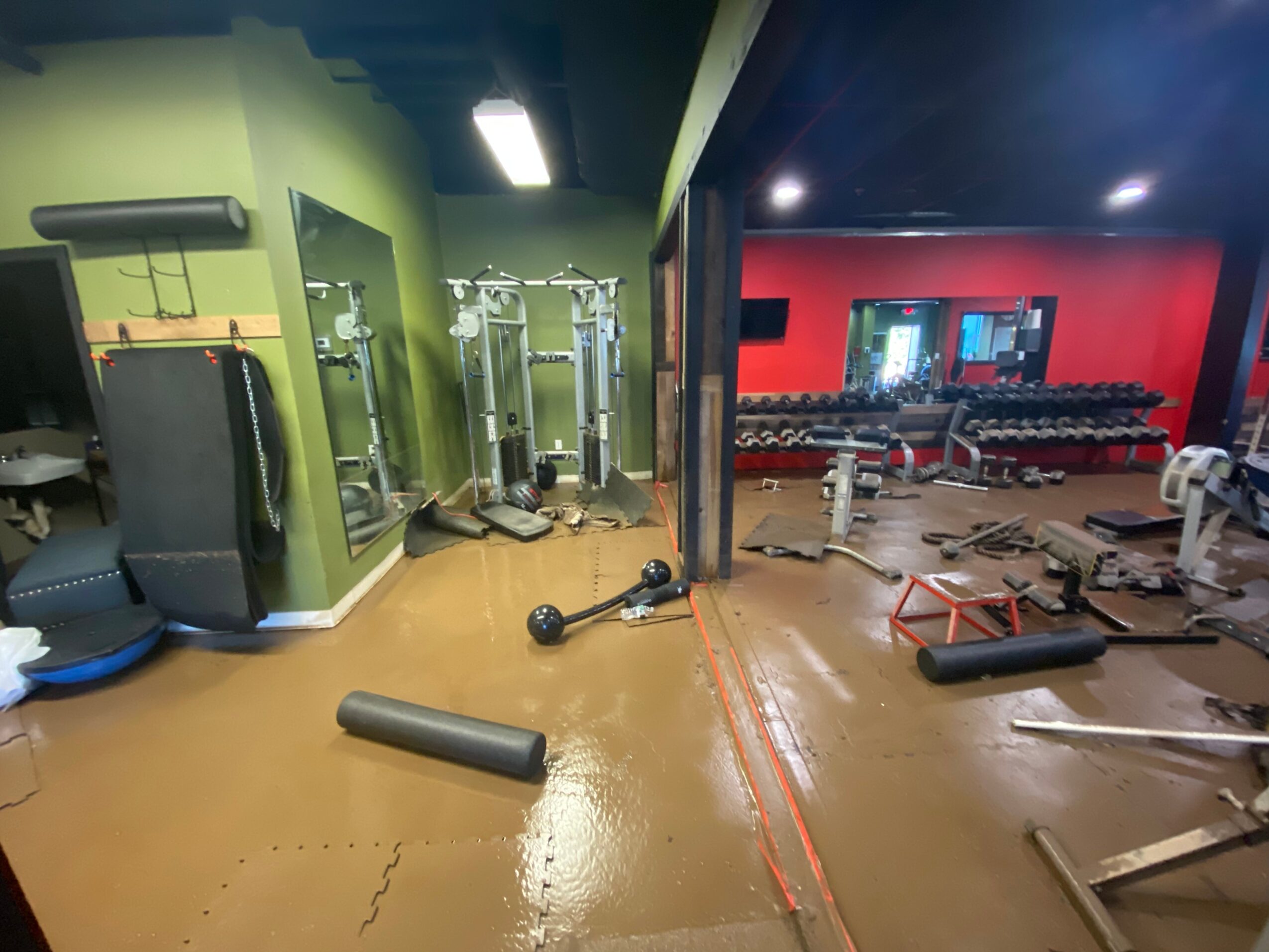 Gym with green and red walls, exercise equipment, and weights, viewed from a side angle.