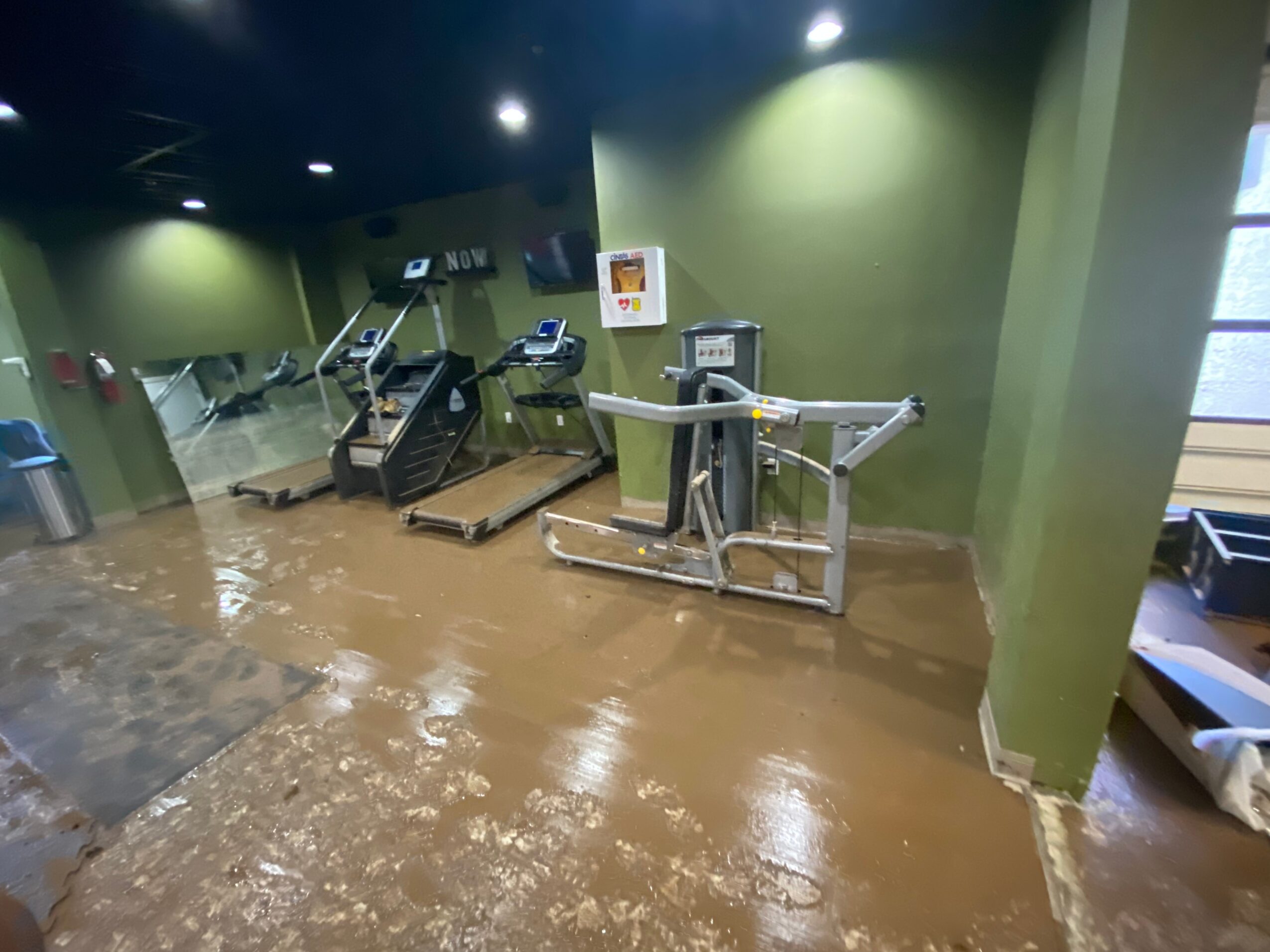 Flooded gym with water covering the floor, exercise equipment partially submerged, and green walls in the background.