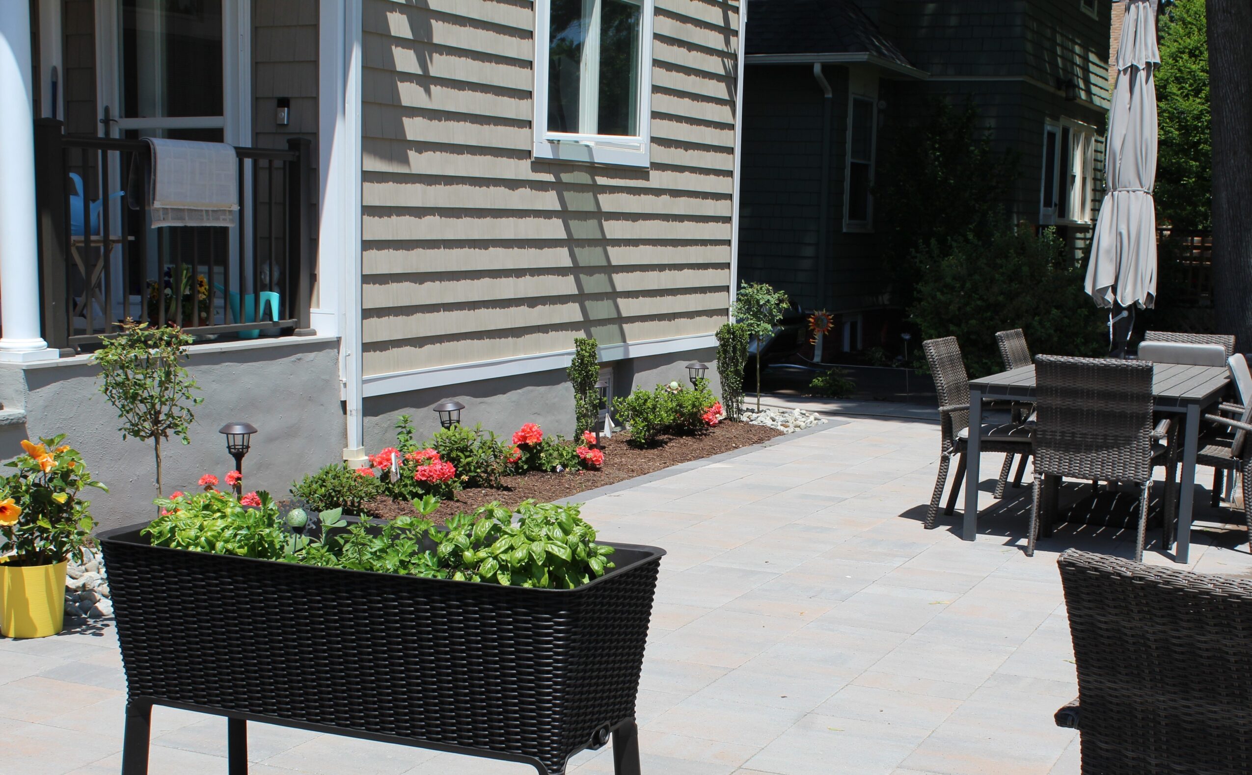 Outdoor patio with black wicker furniture, potted plants, and a house with siding in the background.