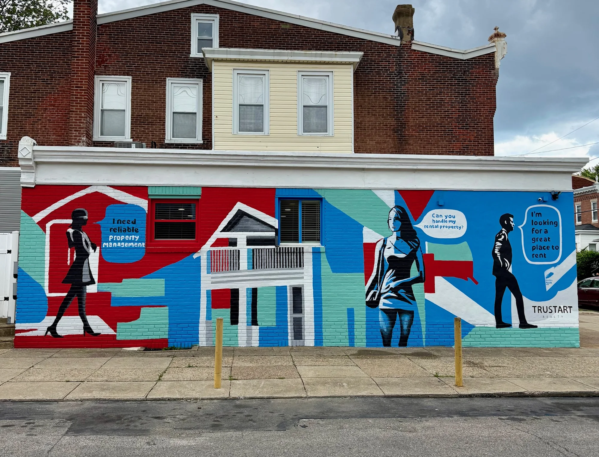 Colorful mural on building wall depicting stylized people and houses with speech bubbles, in red, blue, black, and white.