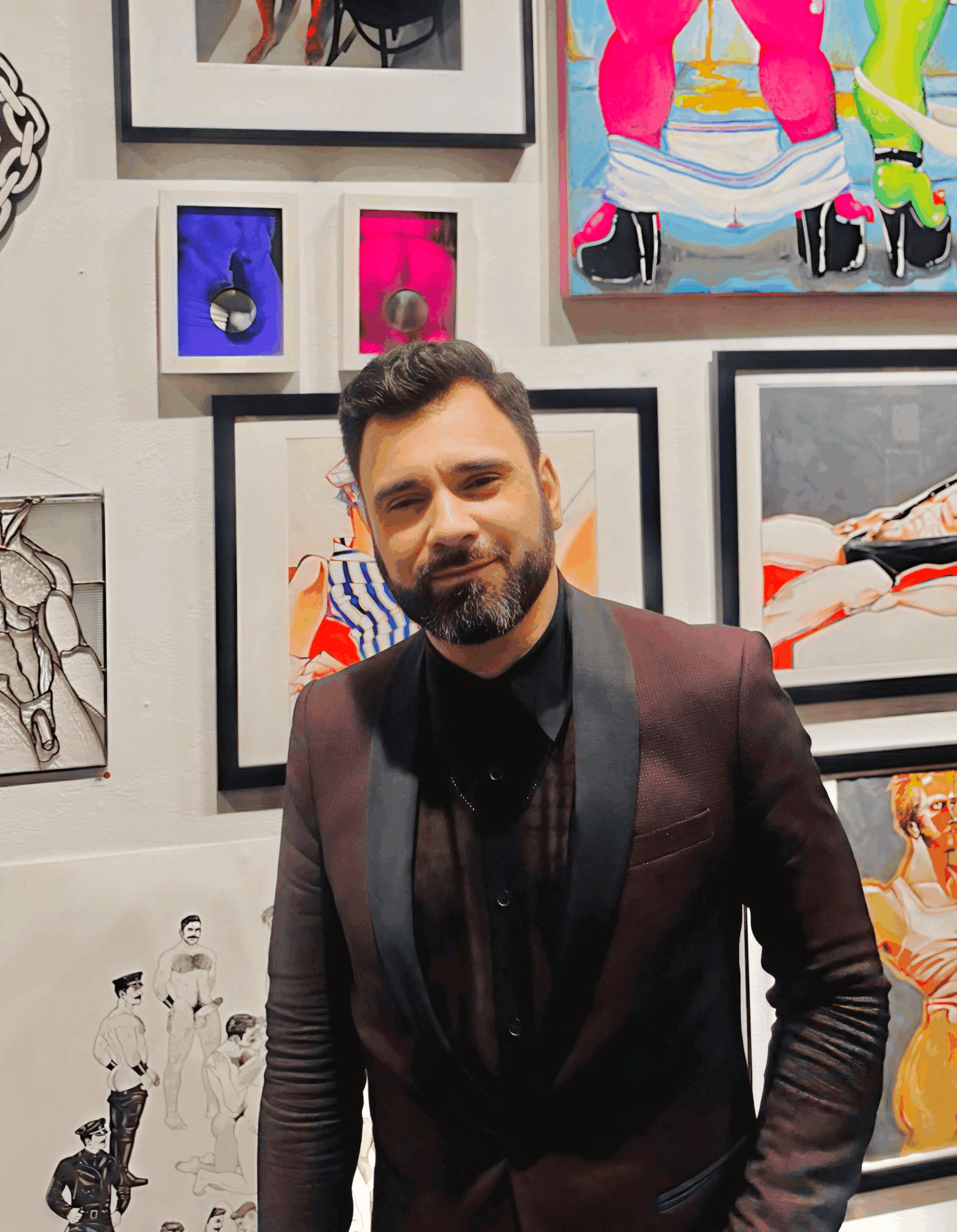 Man with dark hair and beard in a dark suit standing in front of colorful artwork on a wall.
