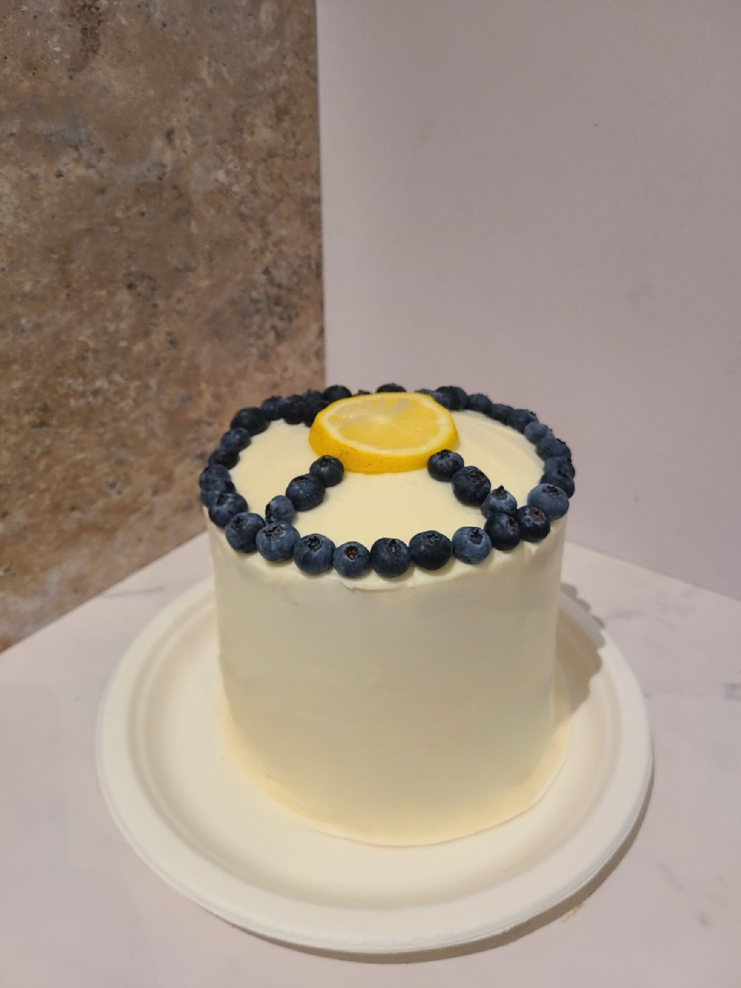 Small round cake with white frosting, decorated with a yellow and black ring on top, on a white plate.