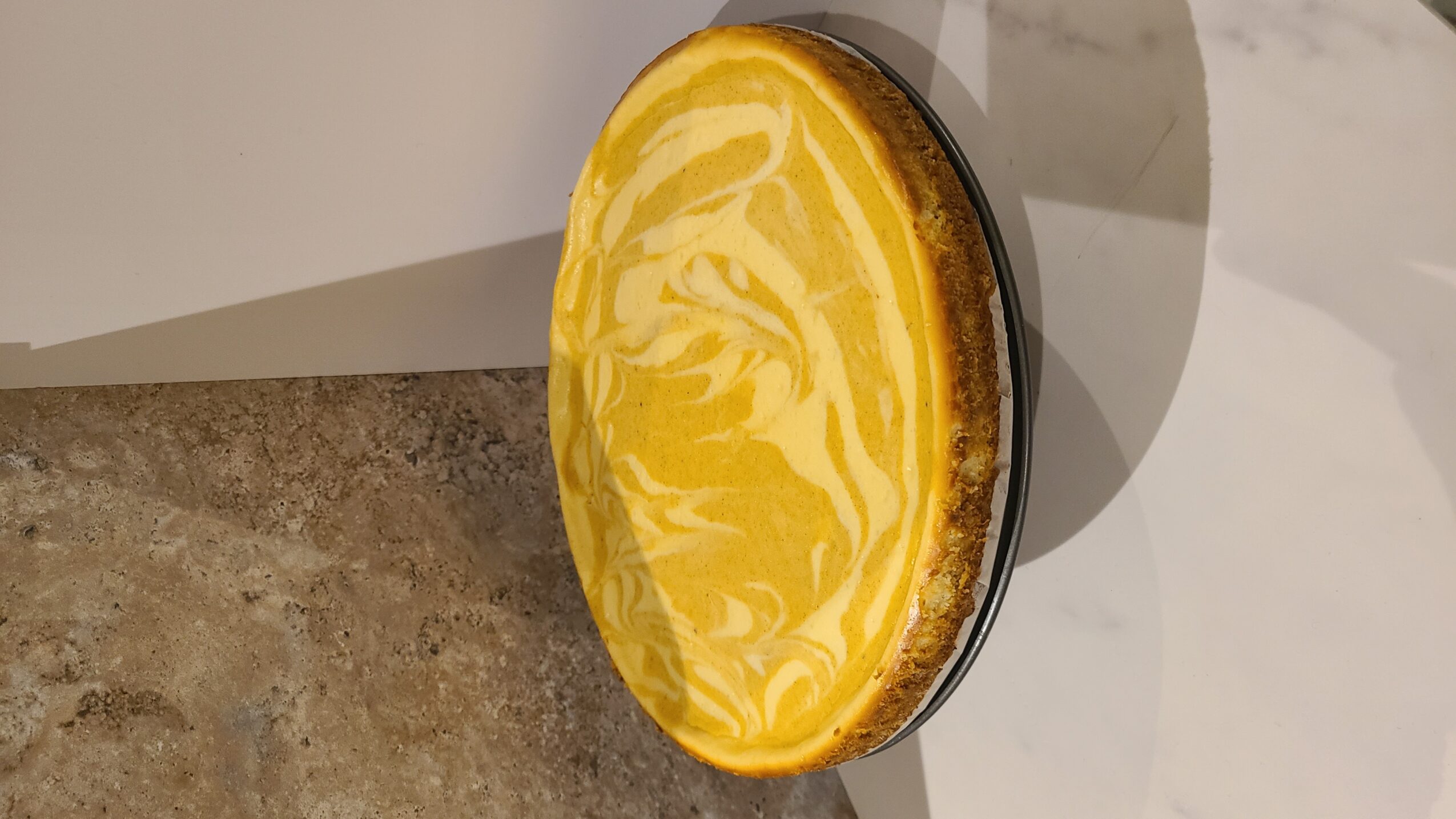 Round lemon tart with a yellow and white marbled filling on a surface, with a plain background.