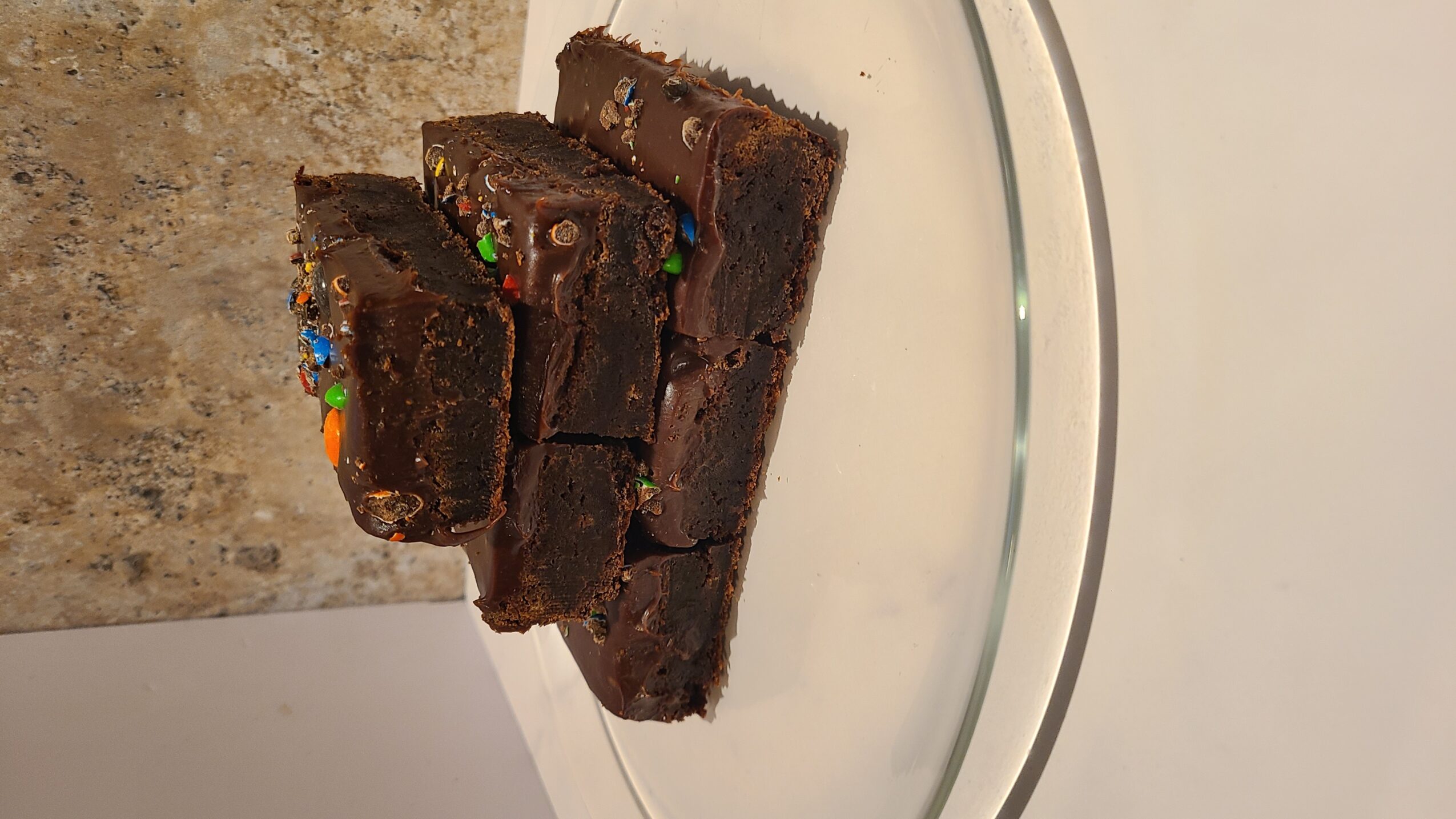 Stack of four chocolate brownies with colorful sprinkles on a white plate.