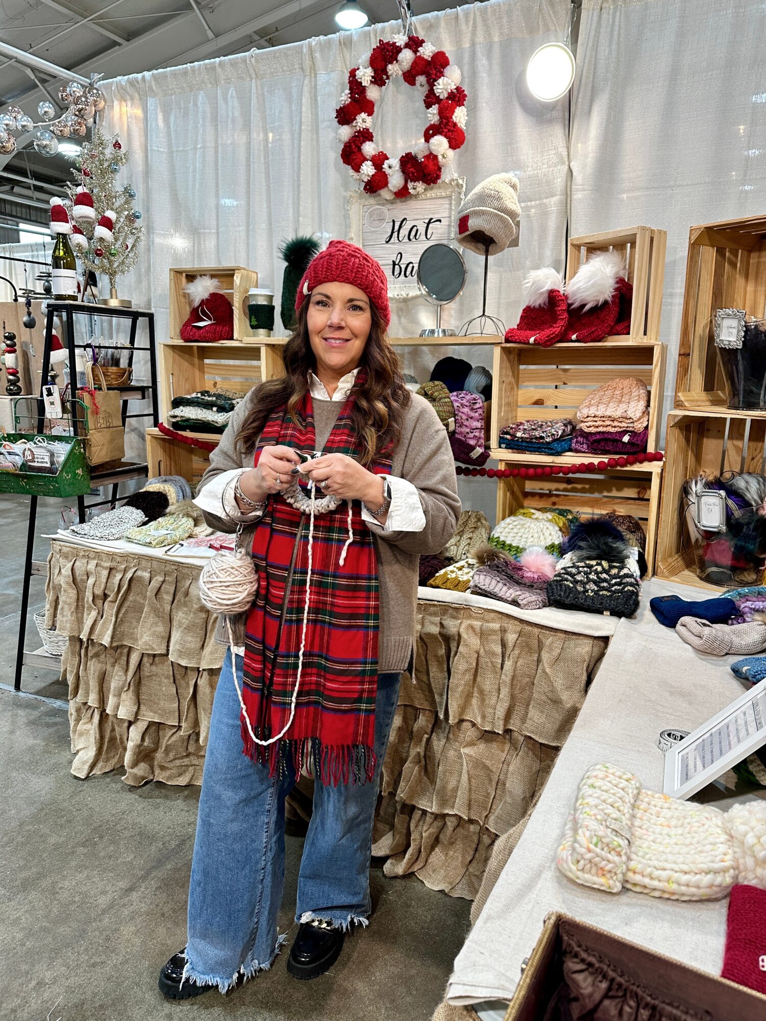 Woman in a red hat and scarf, smiling, standing in front of a holiday display with hats and decorations.