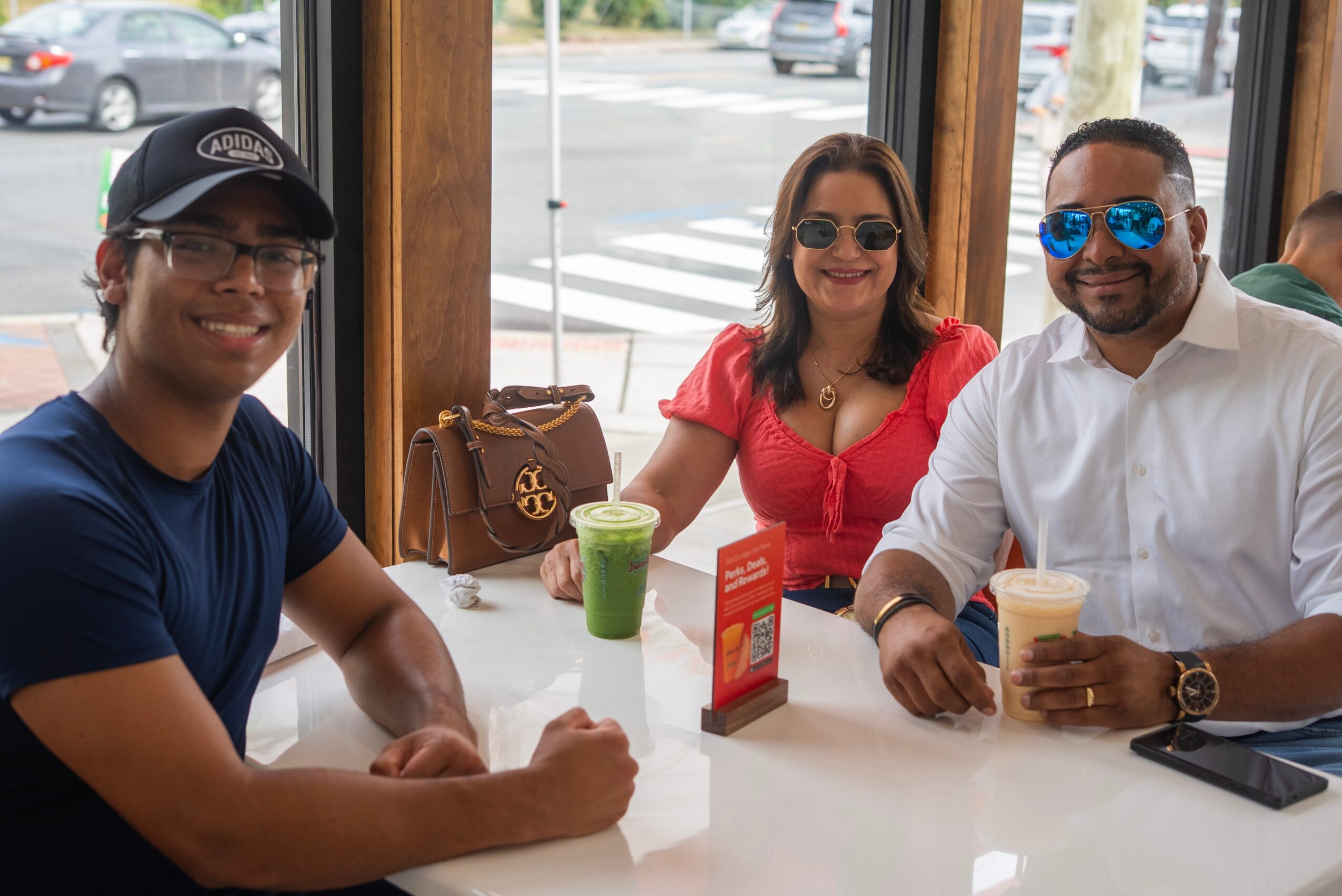 Three people sitting at a table inside a cafe, smiling, with drinks and a purse on the table.