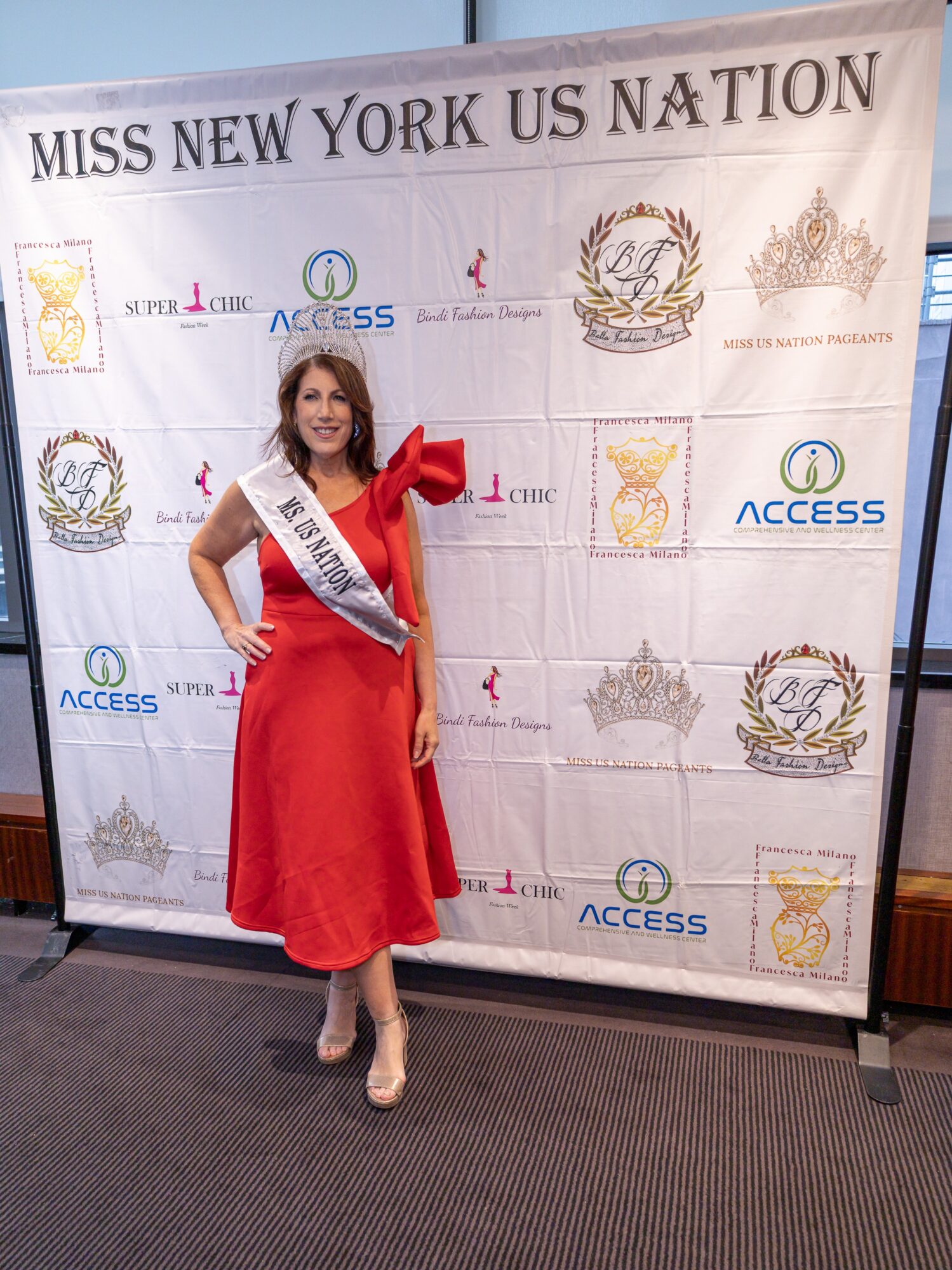 Woman wearing a sash and red dress standing in front of a backdrop with text and logos.