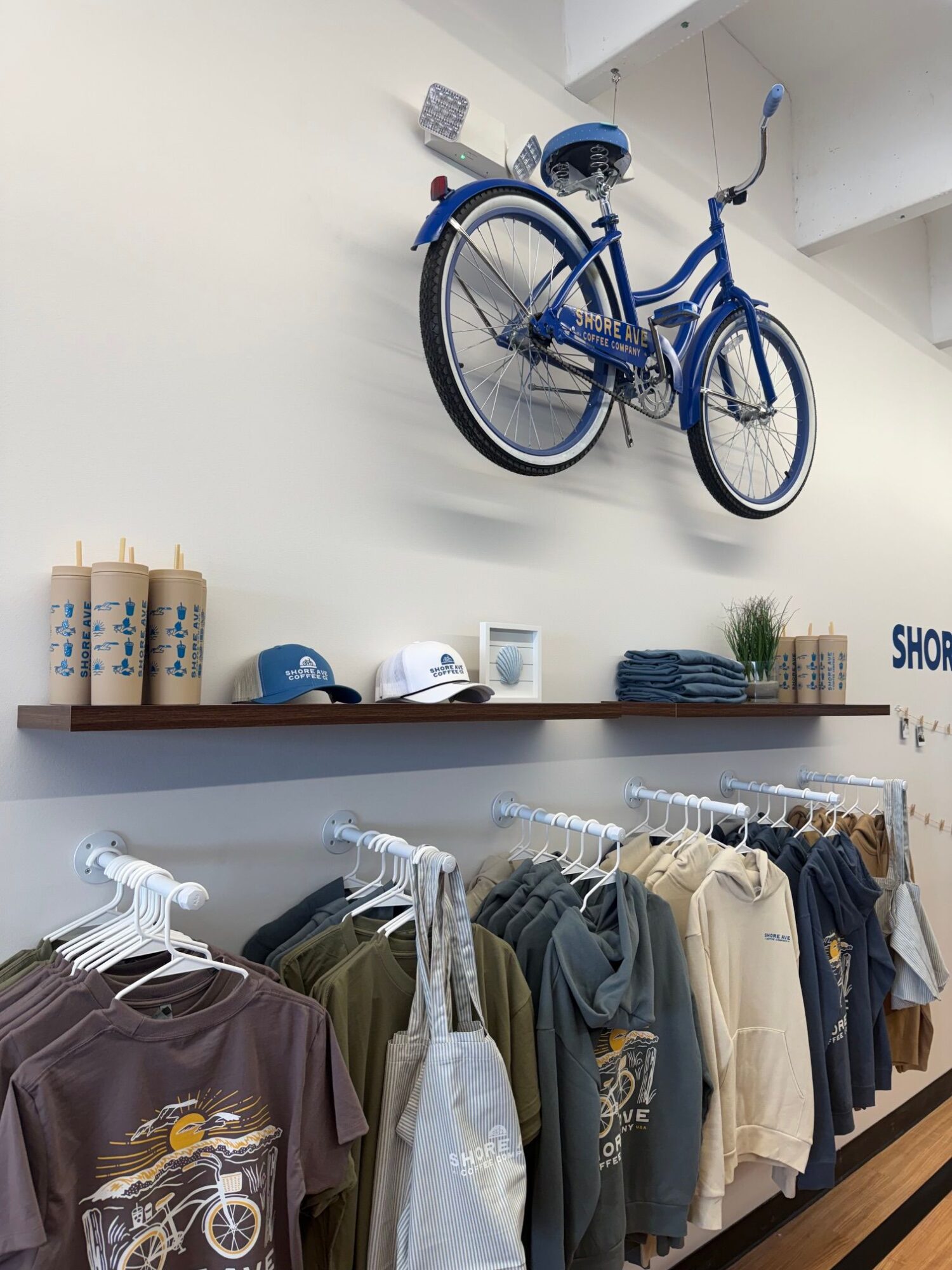 Blue bicycle mounted on a white wall, with clothing racks and shelves below, in a retail store setting.