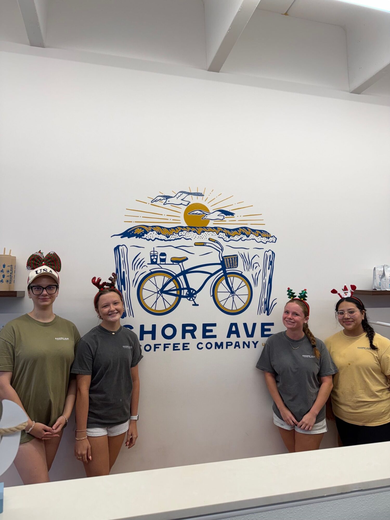 Four people standing and sitting in front of a wall with a logo and text, smiling and posing for the photo.